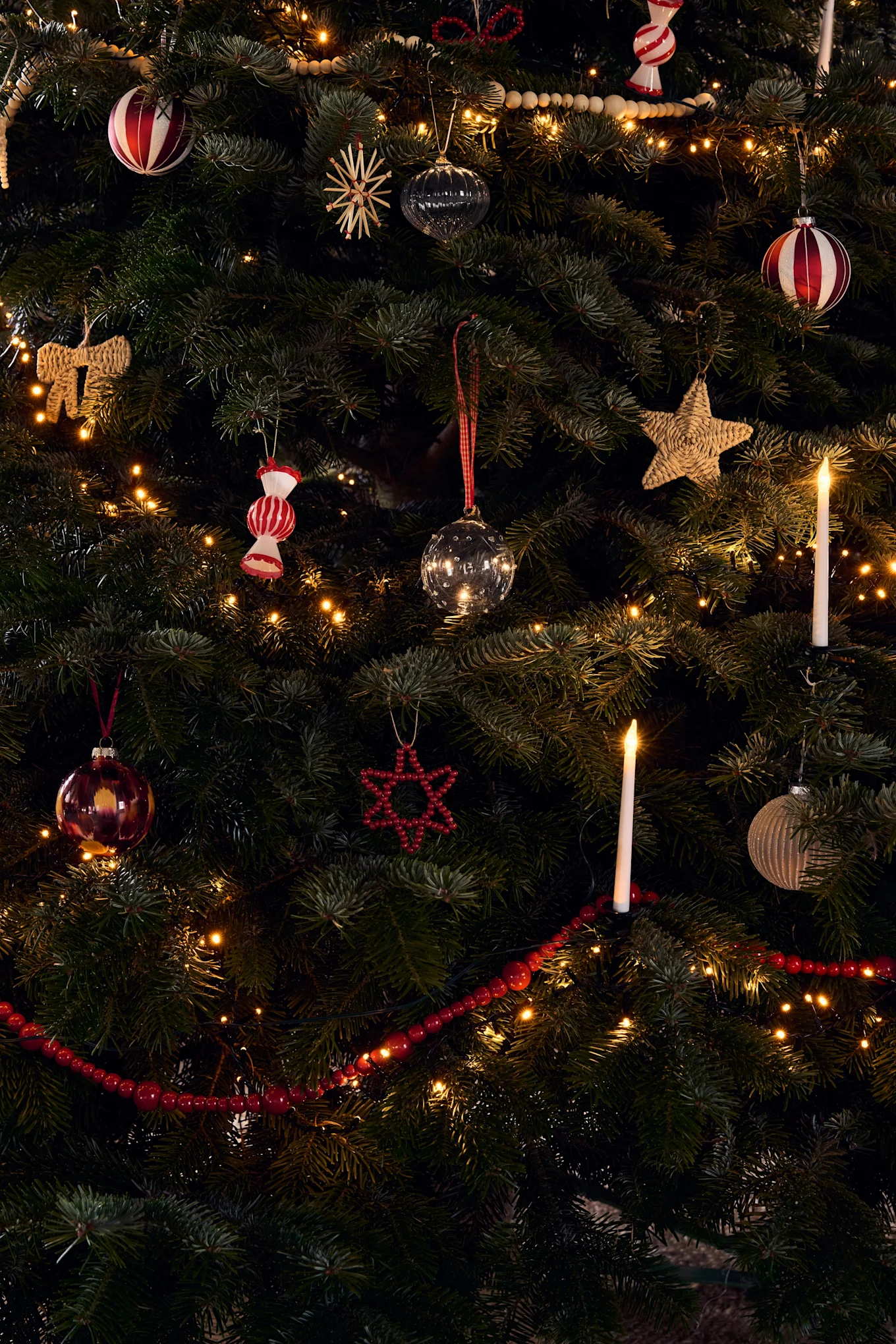 A richly decorated Christmas tree with various ornaments, warm string lights, and glowing candle lights.