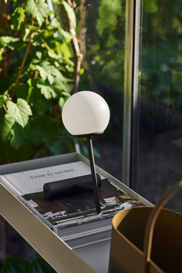 The cordless table lamp Phare from Menu in a greenhouse resting on a book.