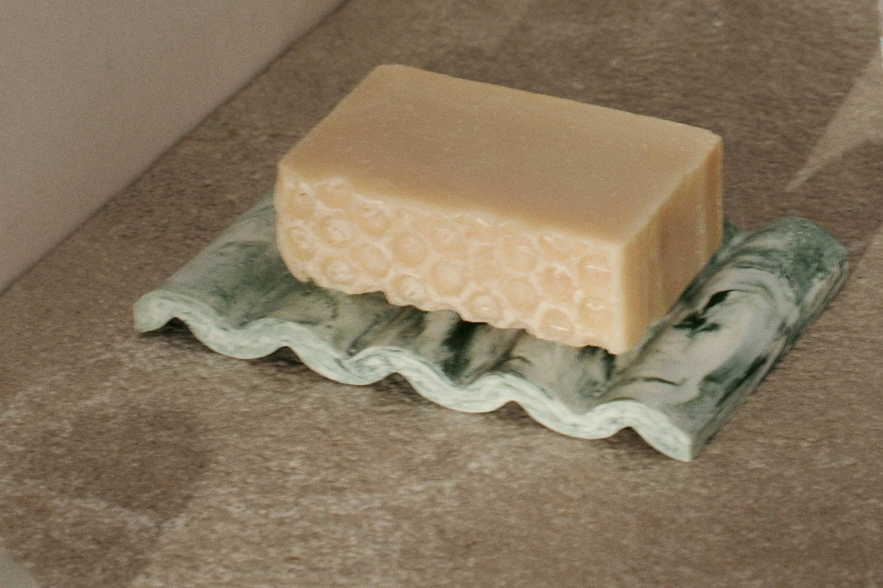 Light beige soap bar with honeycomb texture on a wavy green marbled soap dish.