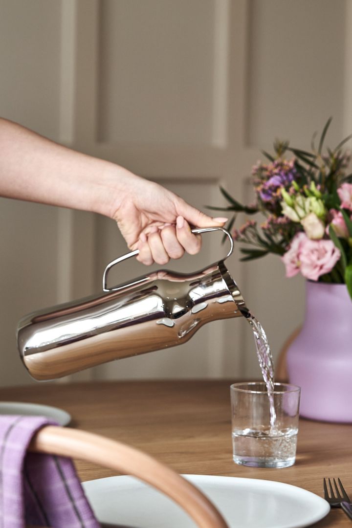A hand pours water from the Dorotea water jug in polished stainless-steel. 