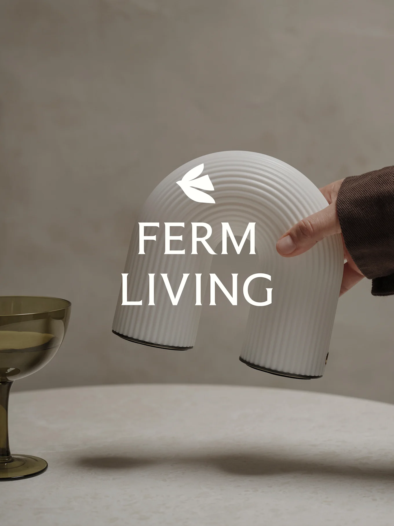 Hand holding a white ribbed arch-shaped decorative object, with a green glass nearby.