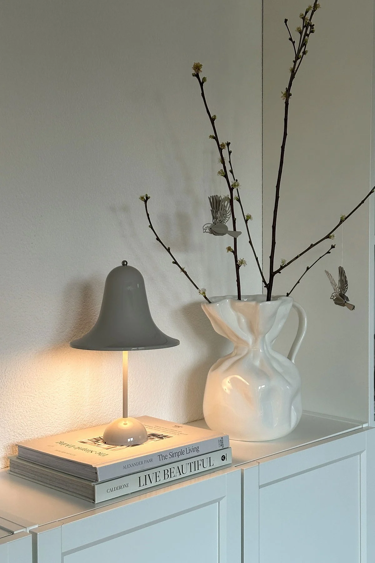 At @oursmall.home you can see two possible Mother's Day gifts: the Pantorp table lamp from Verpan stands on a chest of drawers, next to it the Crumple vase from Byon with a few twigs in it.