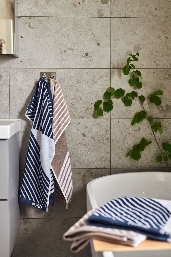 Blue and beige striped towels from NJRD hanging in a beige tiles bathroom. 