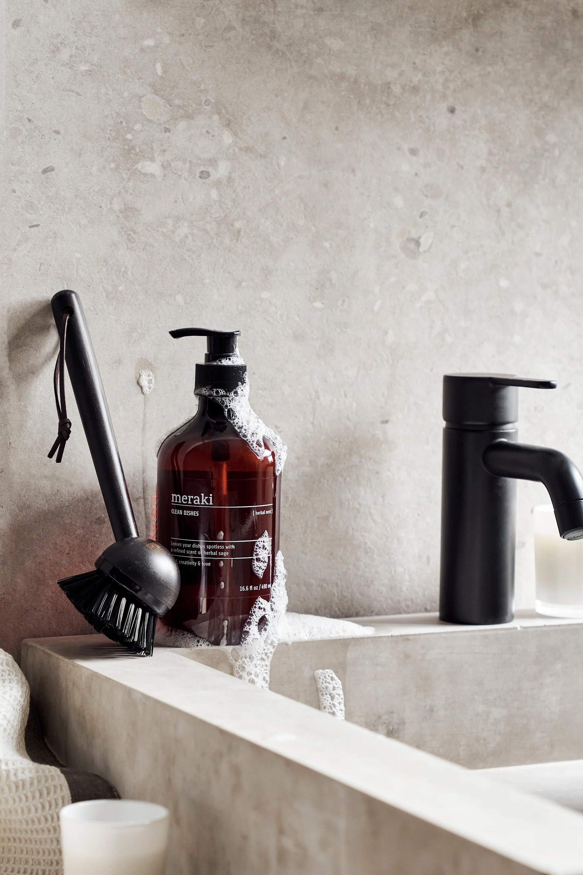 The Meraki gift set, consisting of washing-up liquid and dishwashing brush, stands on a sink.