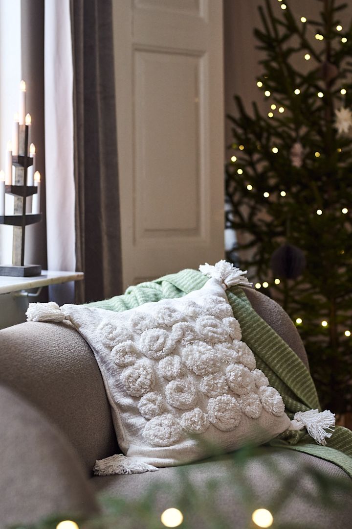 A white pillow with tassels and a green throw on the sofa for a modern and minimalist Christmas decor this year.