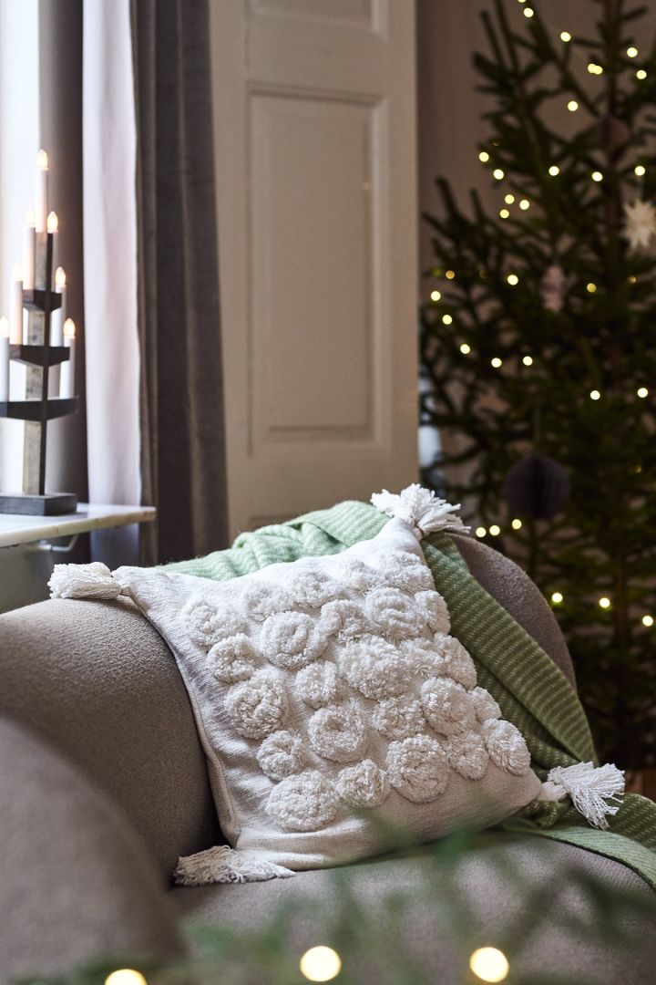 A white pillow with tassels and a green throw on the sofa for a modern and minimalist Christmas decor this year.