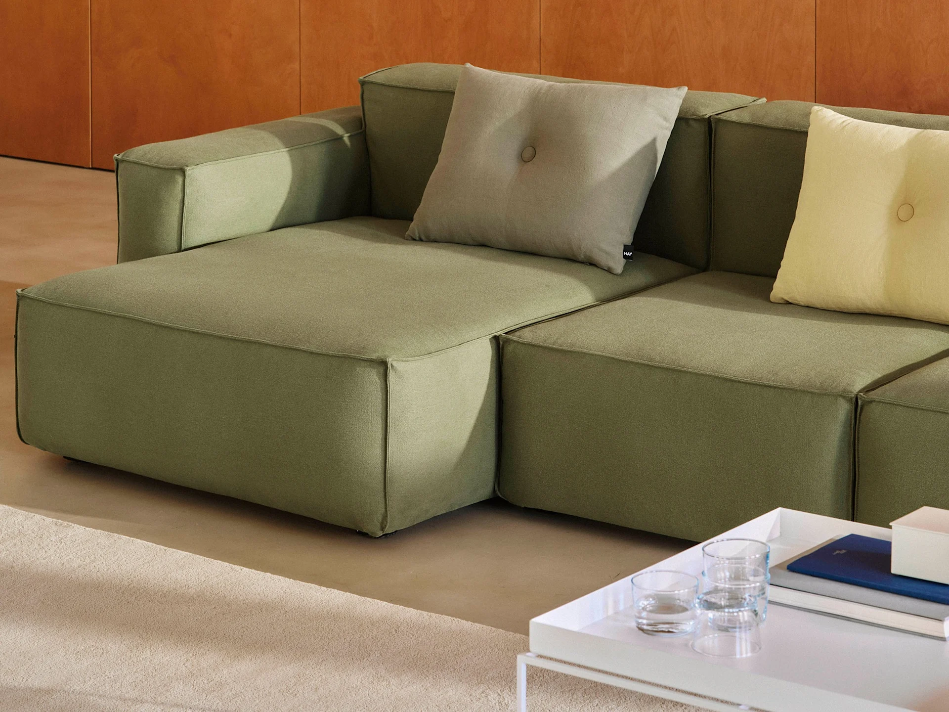 A modular olive green sofa with light grey and yellow throw pillows, next to a white coffee table with books.