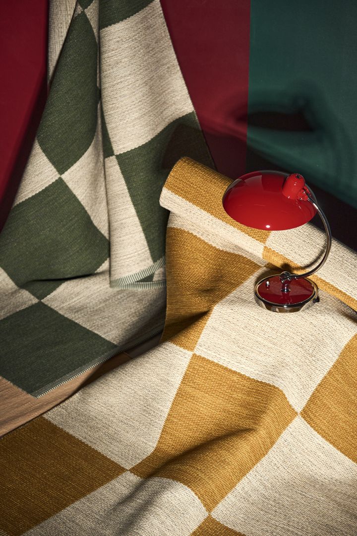 Geometrically patterned rugs in mustard yellow/white and green/white are just right for 2024 interior design trends in Scandinavian, here with a red table lamp next to them.  