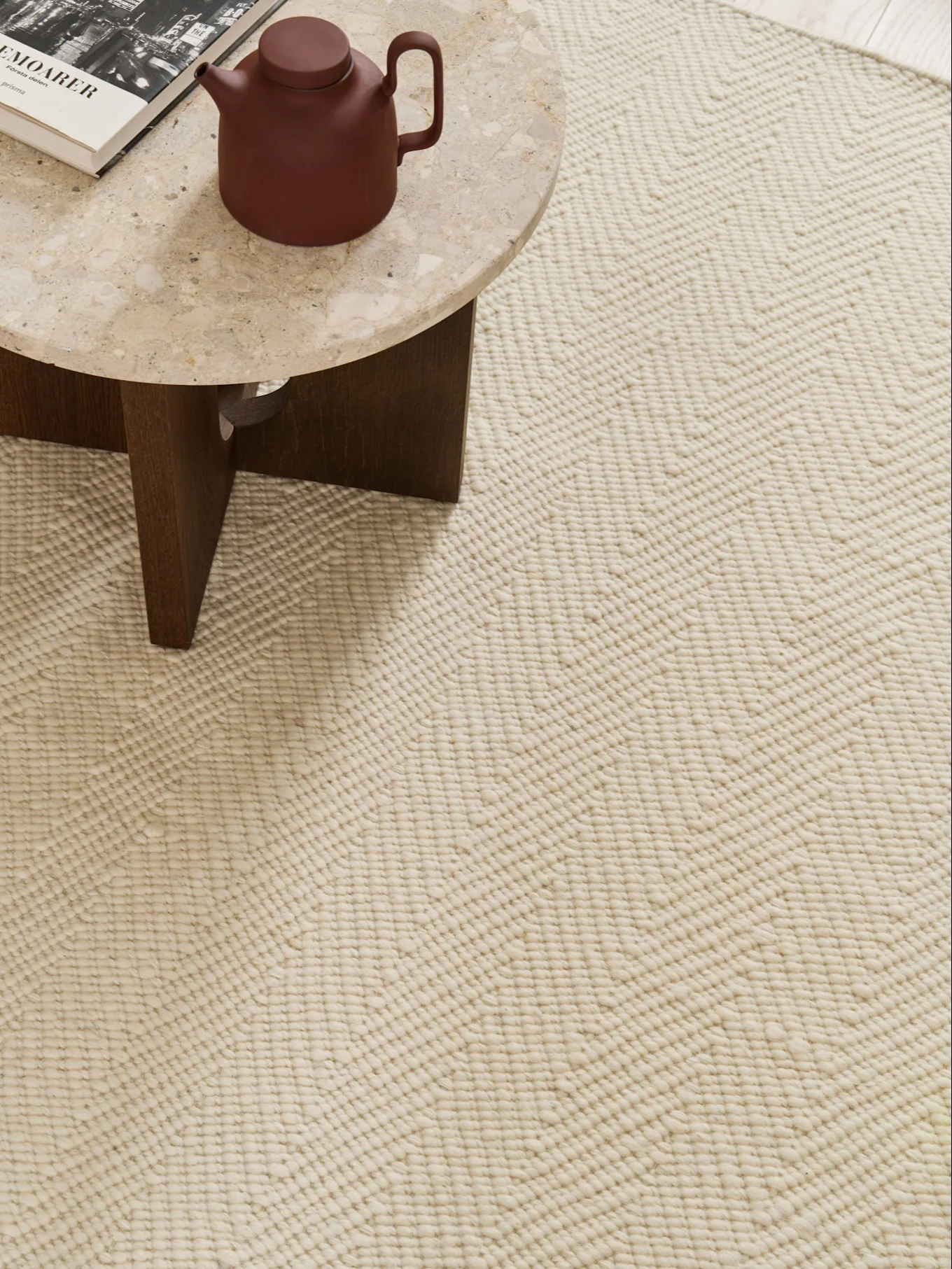 Close-up of a cream rug with a textured zigzag pattern, with a marble table holding a teapot and book in the corner.