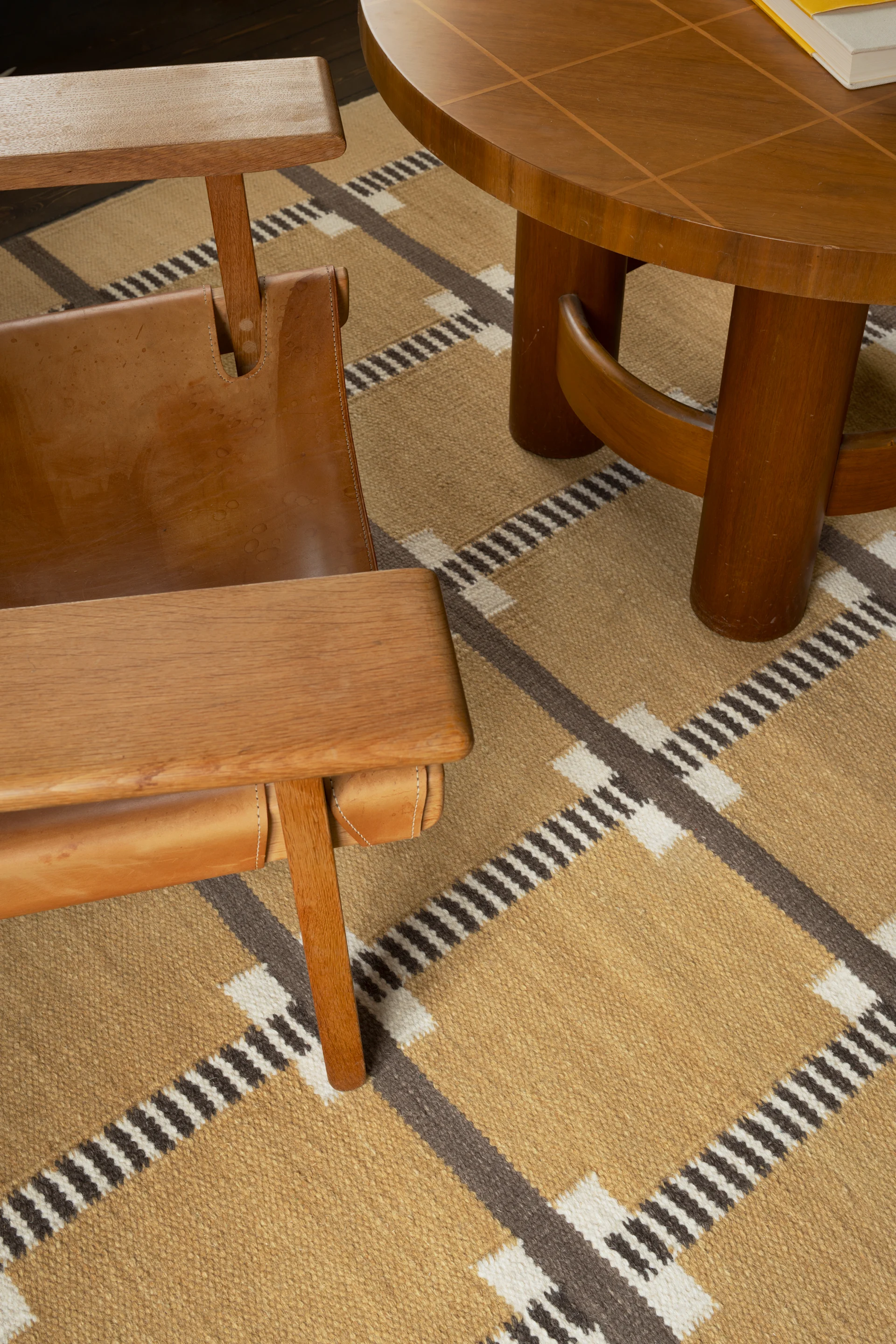 Wooden armchair with leather seat next to a round coffee table on a geometric patterned rug.