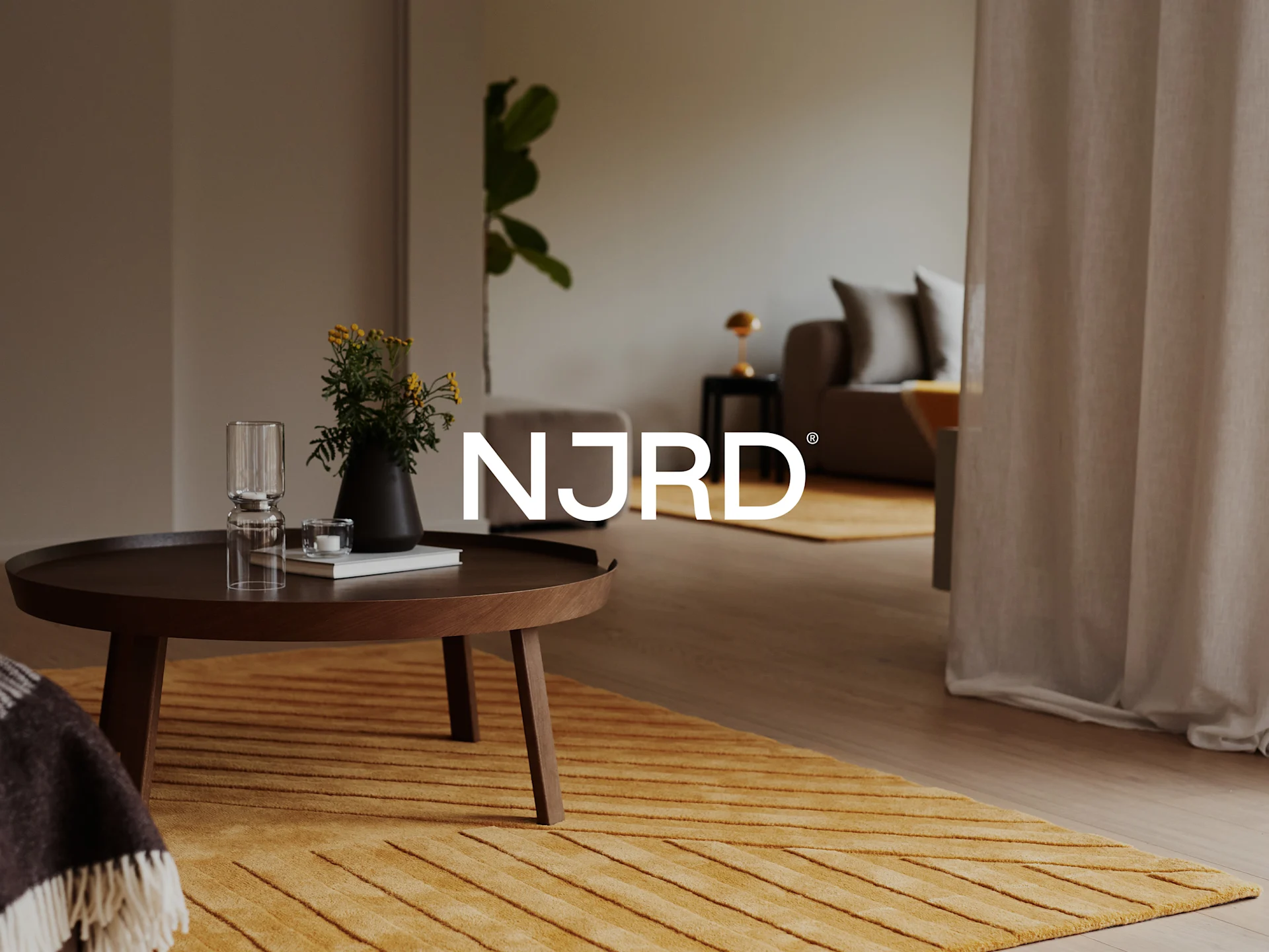 A cozy living room featuring a round wooden coffee table with flowers and a glass, and a textured yellow rug.