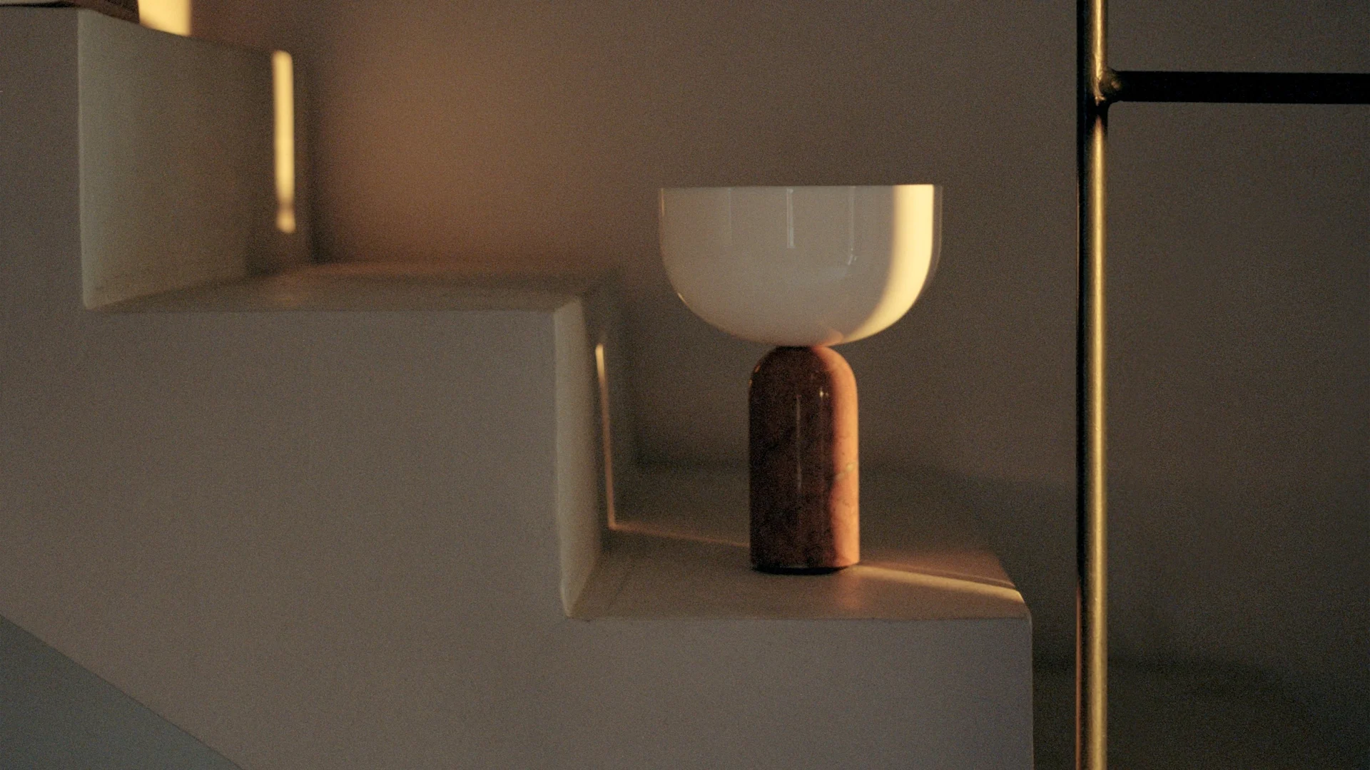 Modern lamp with a white bowl top and a reddish-brown cylindrical base on white stairs, bathed in warm sunlight.