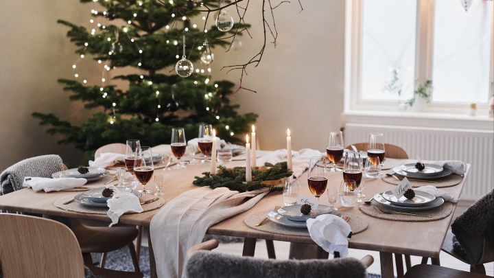 A white and minimalist Christmas table setting for this year's Christmas dinner with natural decorations such as cones and pine cones on the table.