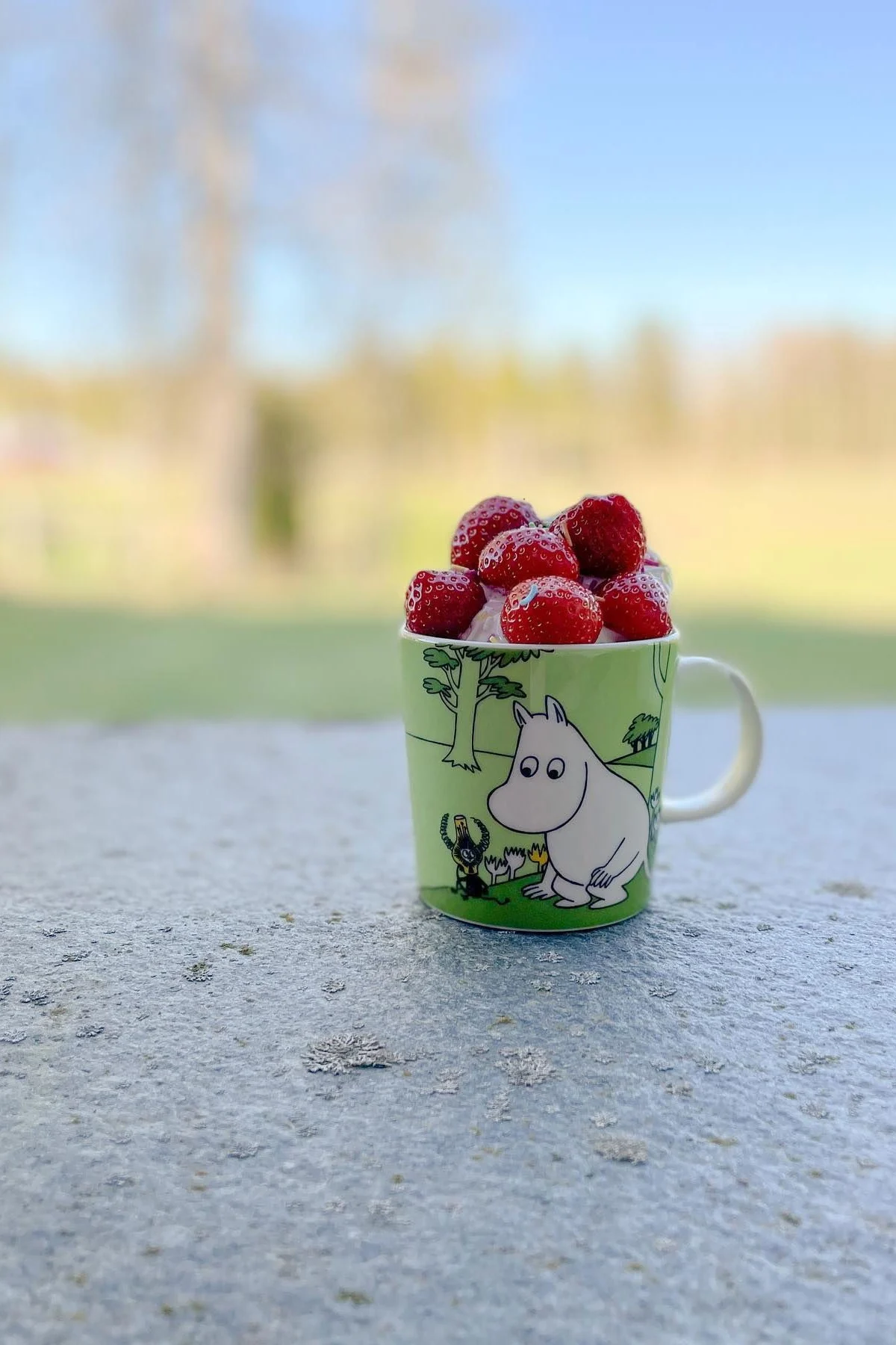 The green Moomin cup from @mylittlemoominfamily is outside on the floor, filled with strawberries.