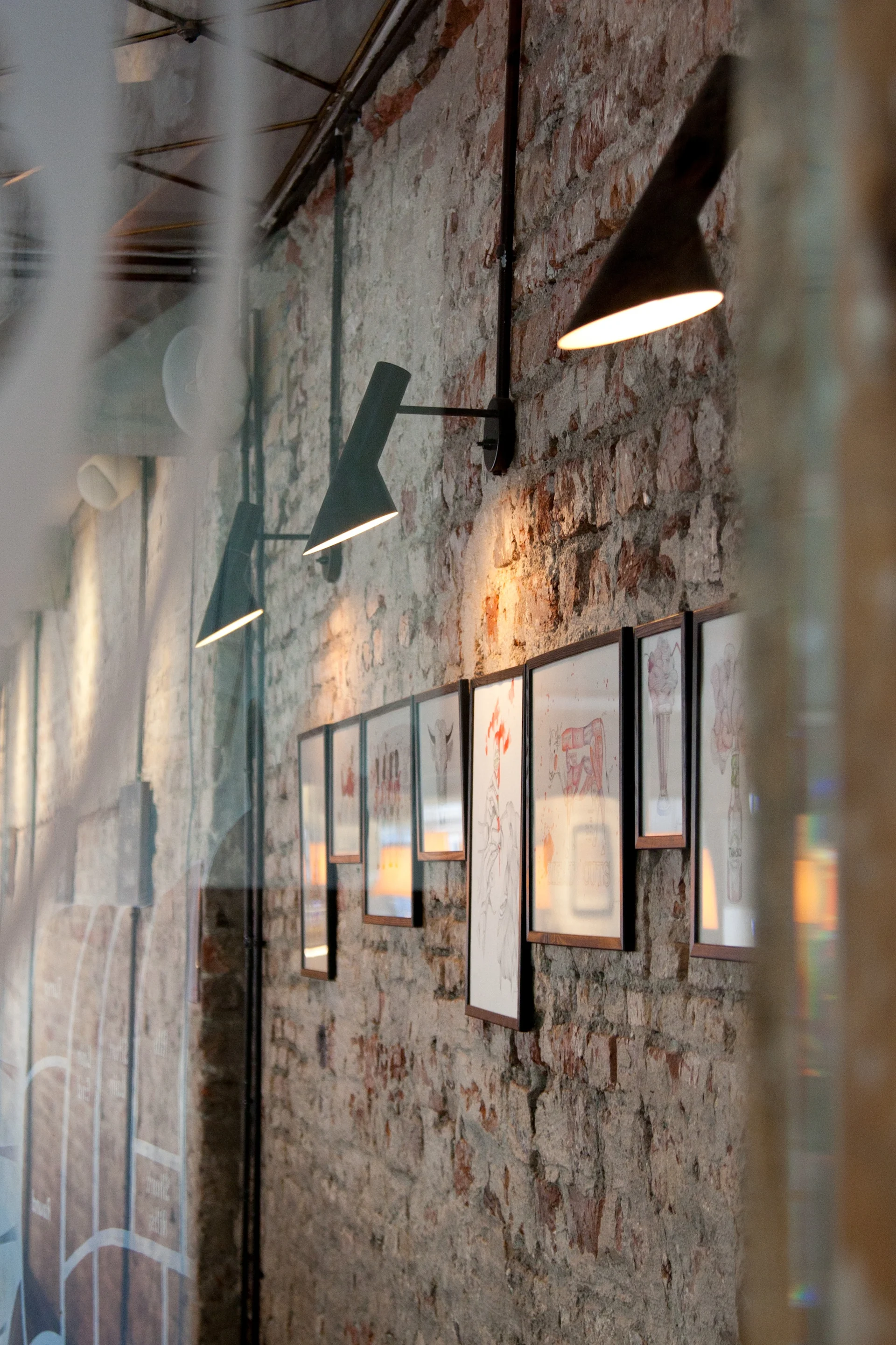 An old brick wall adorned with modern black sconce lights and a row of framed art depicting meat cuts.