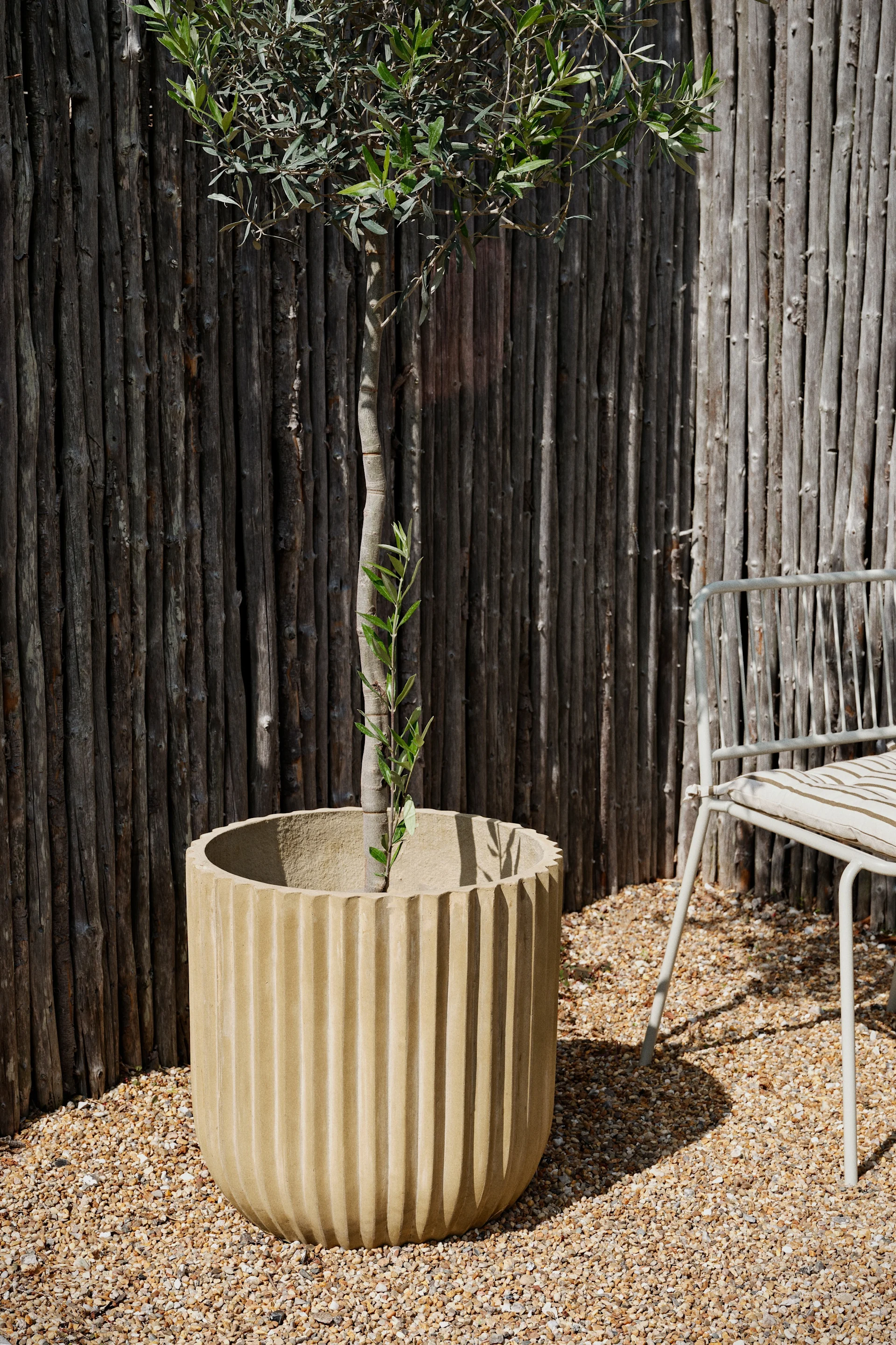 The rustic fibre outdoor planter from Broste Copenhagen stands in a garden.