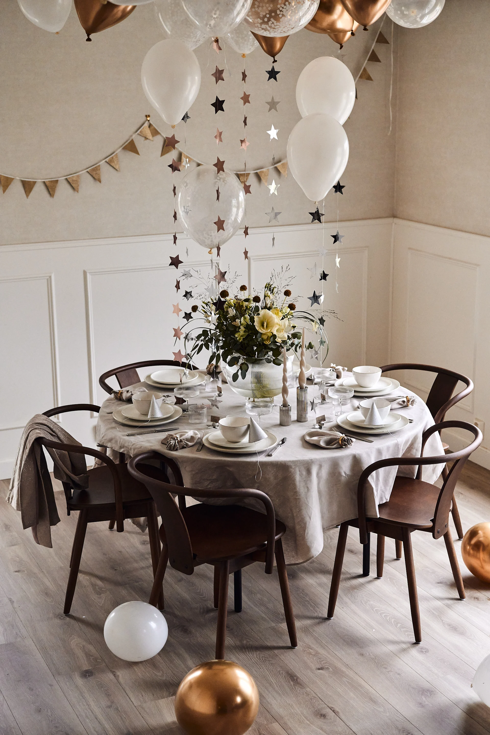 New year party ideas - decorate the table with balloons and hanging stars in a simple colour scheme of white and gold.