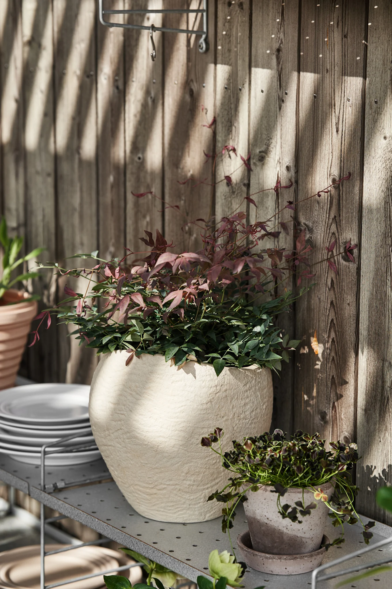 A string shelf on a terrace, on which the large Plantas flower pot from Audo Copenhagen stands.