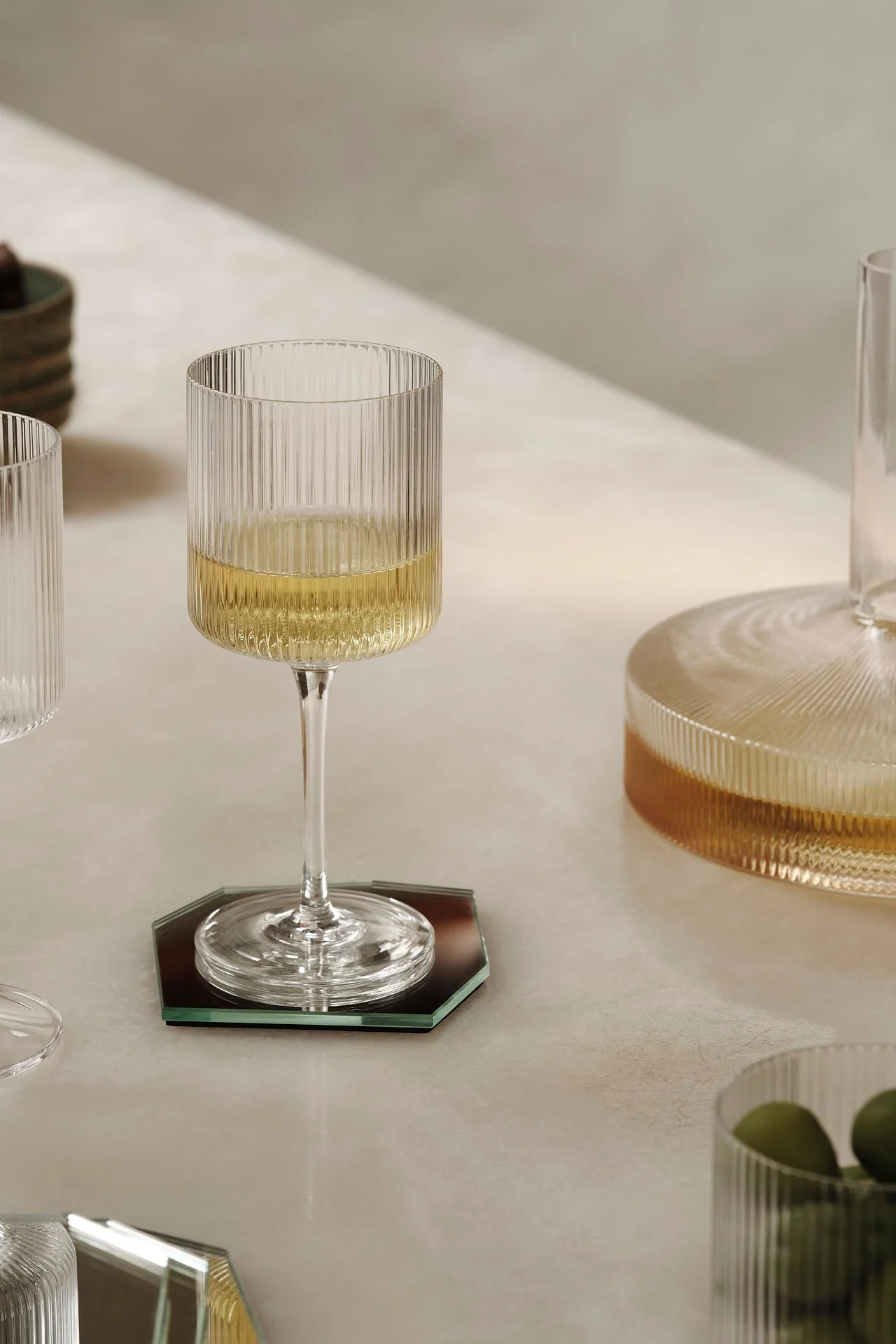 A ribbed wine glass with white wine on a hexagonal mirrored coaster.