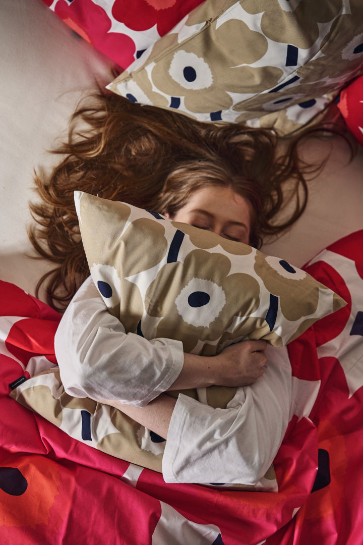 A woman hugs the Unikko pillow in bed surrounded by Unikko bedding in red and pink. 