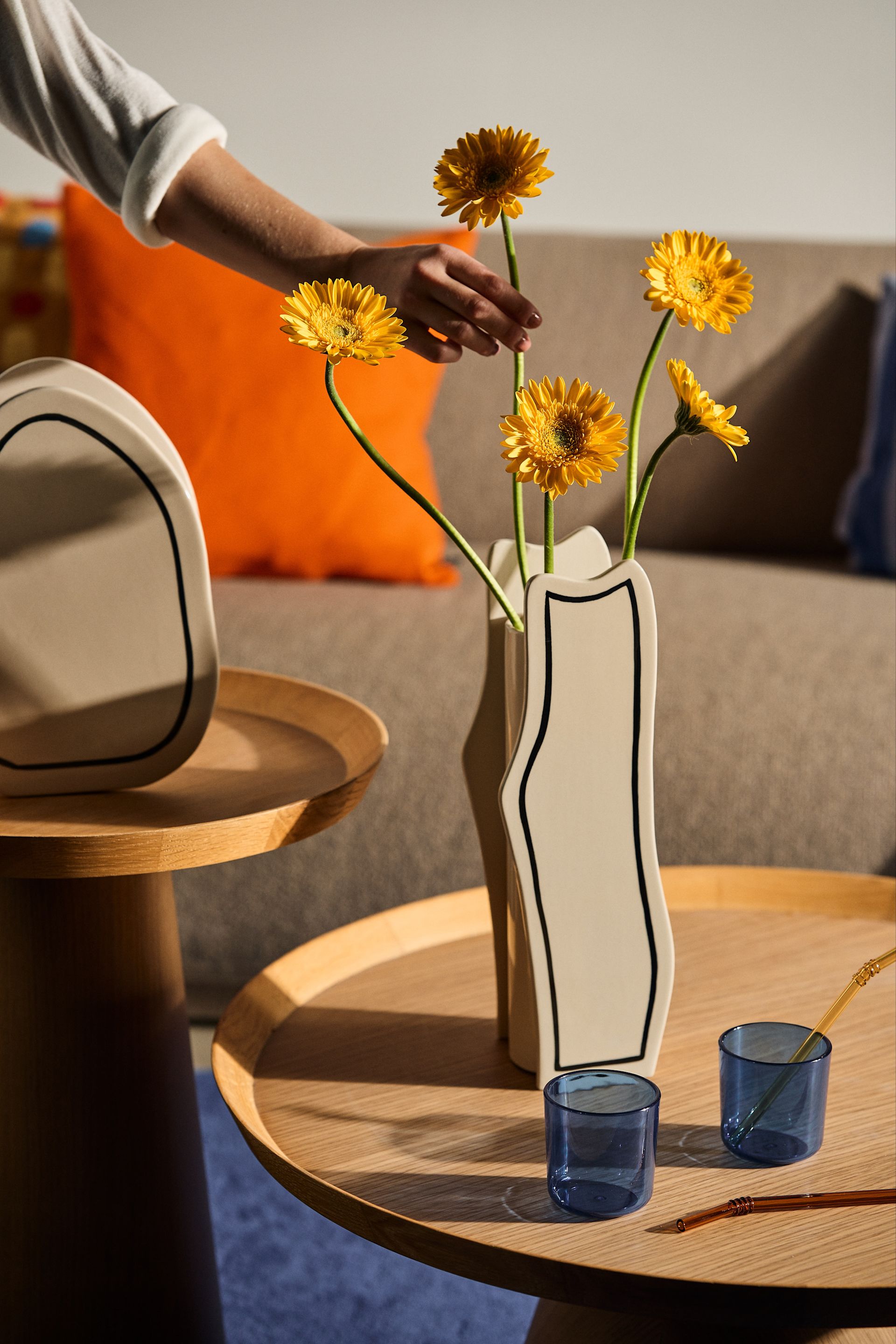 Among the 2024 Scandinavian Interior Design Trends, We see a lot of playful shapes with retro vibes. Here, A Black and White Vase from Ferm Living with Yellow Flowers.