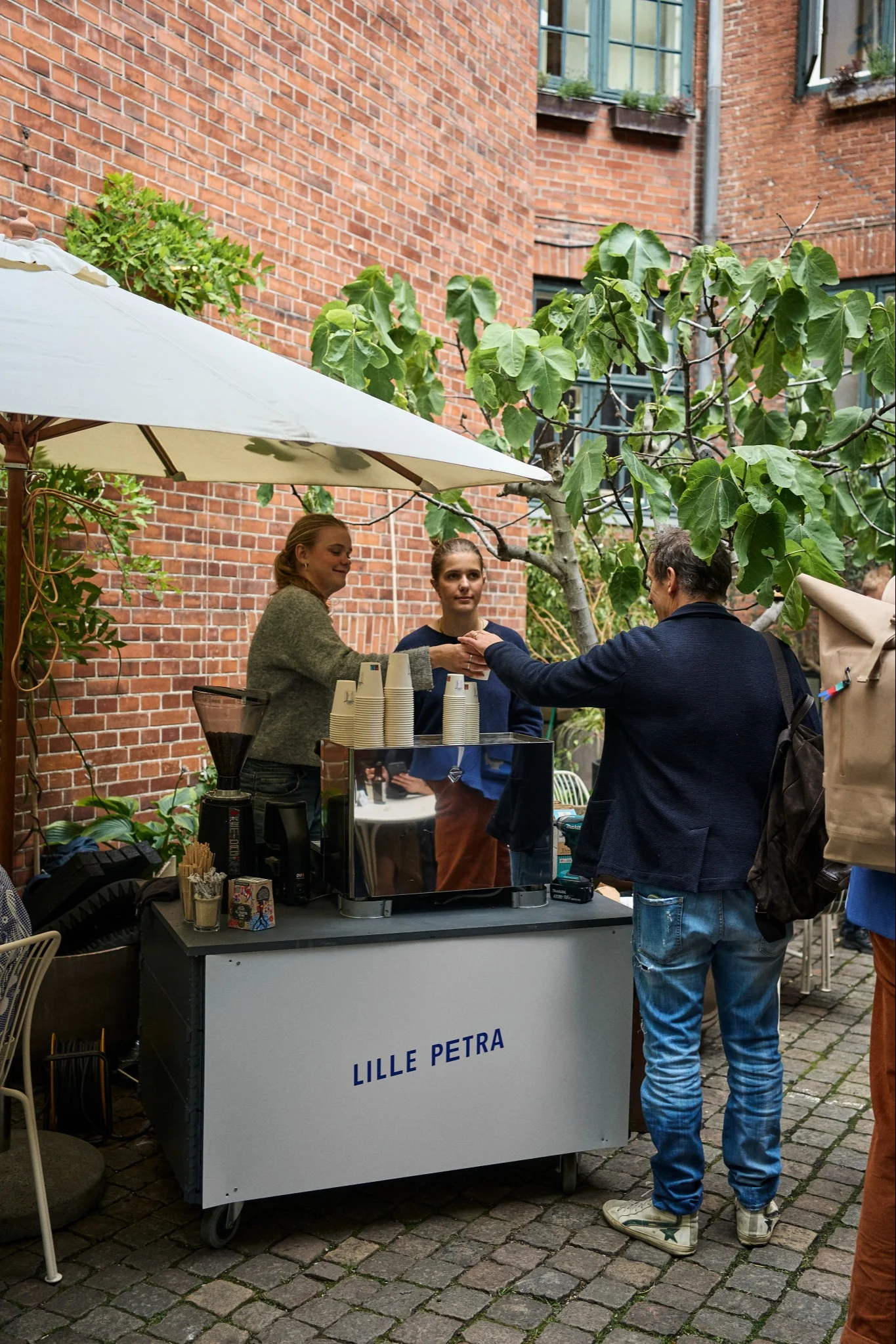 Stop at the Lille Petra Cafe on your Copenhagen city tour for design lovers. Here you see staff handing out coffee in the courtyard.