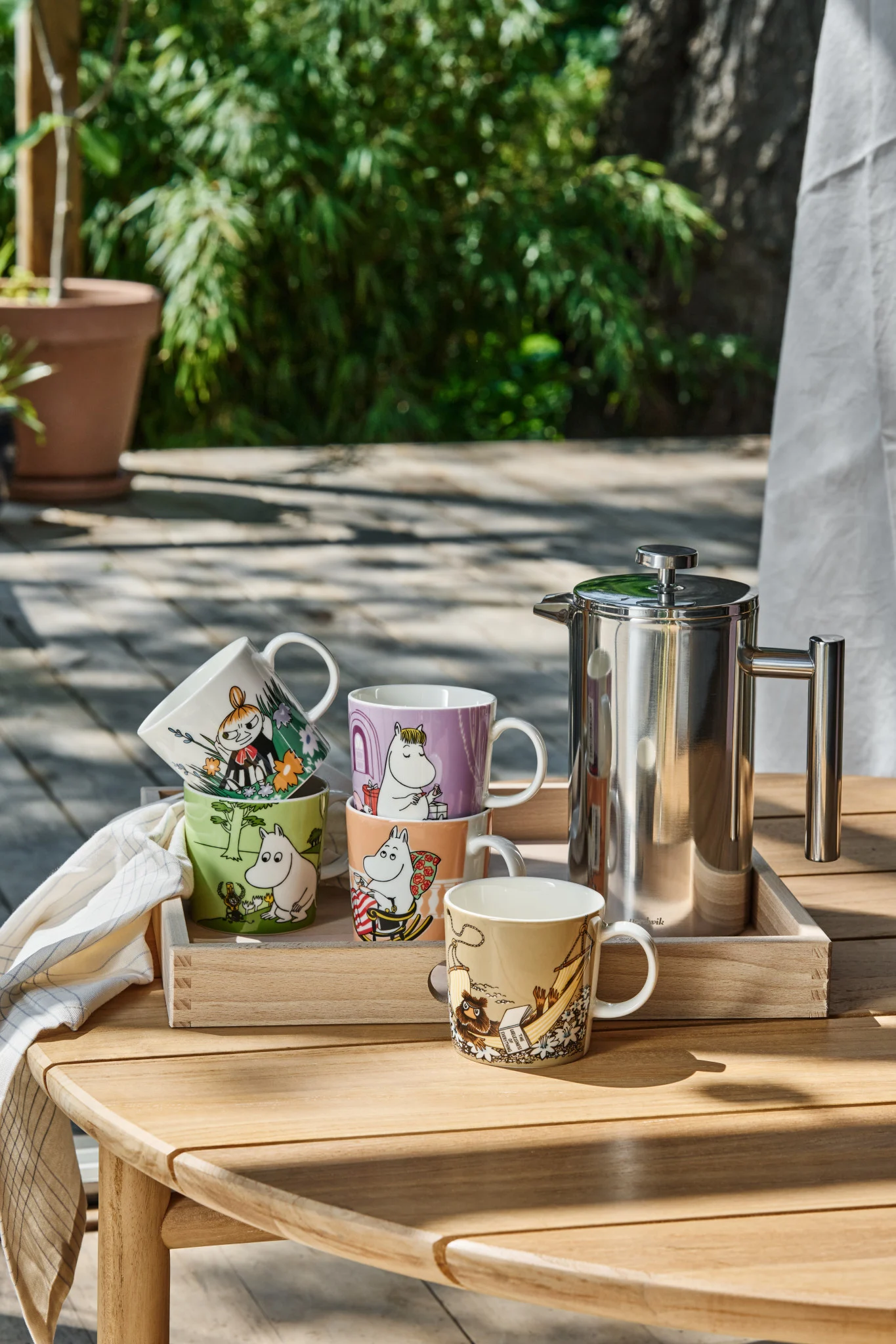 Several Moomin cups stand on a table in the garden.