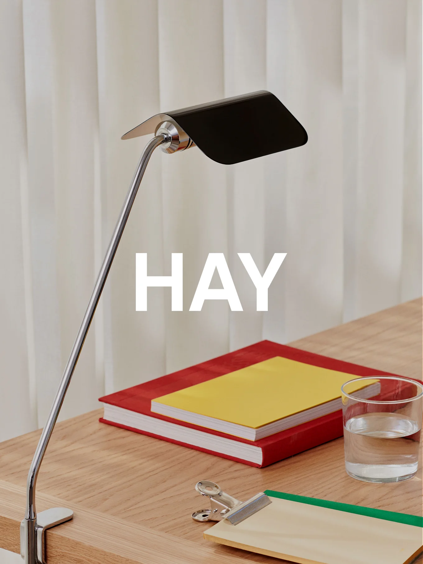 A chrome desk lamp with a black shade illuminates a wooden desk with two books, a glass of water, and a clipboard.