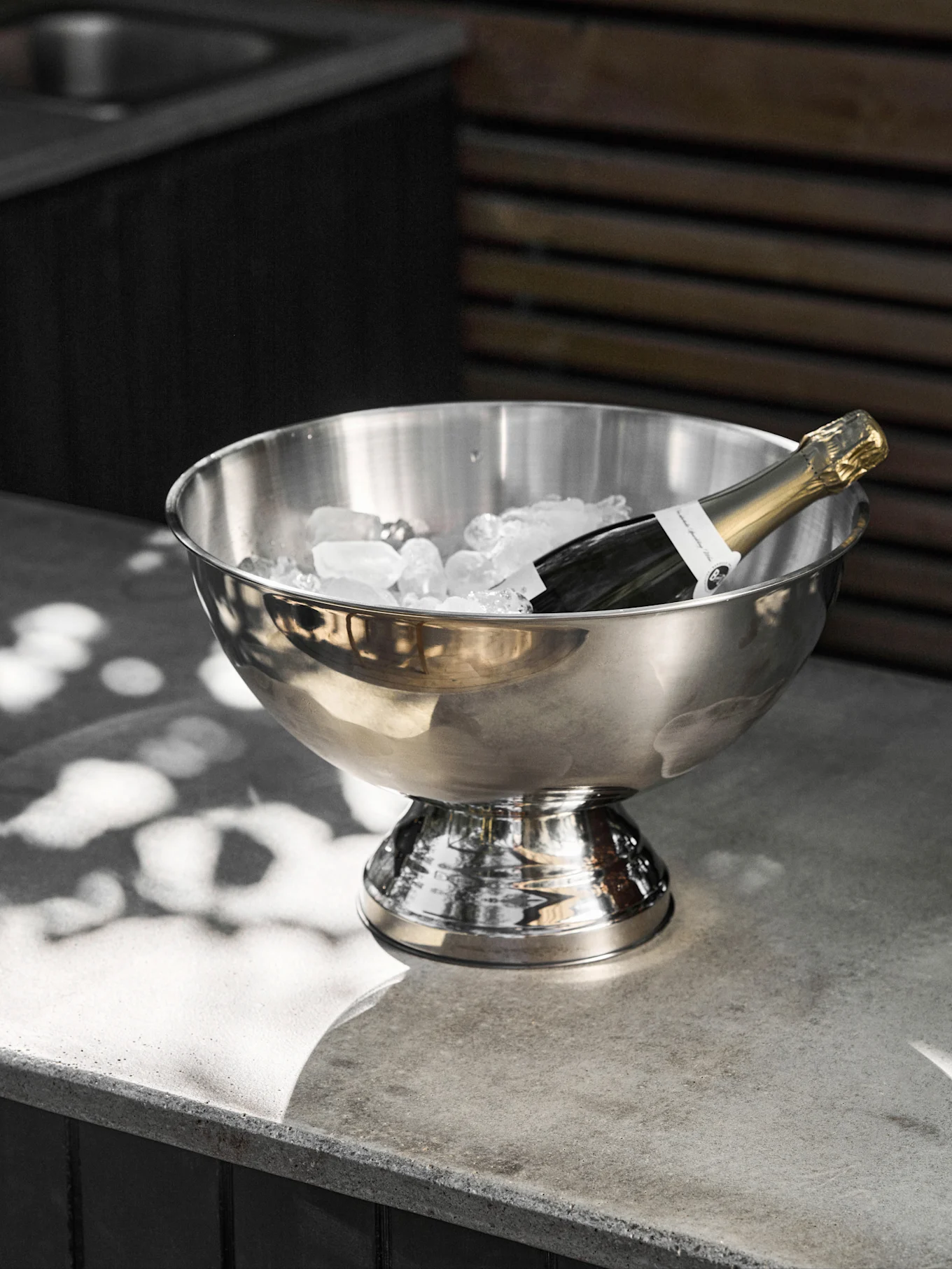Champagne bottle chilling in a stainless steel ice bucket on a concrete surface.