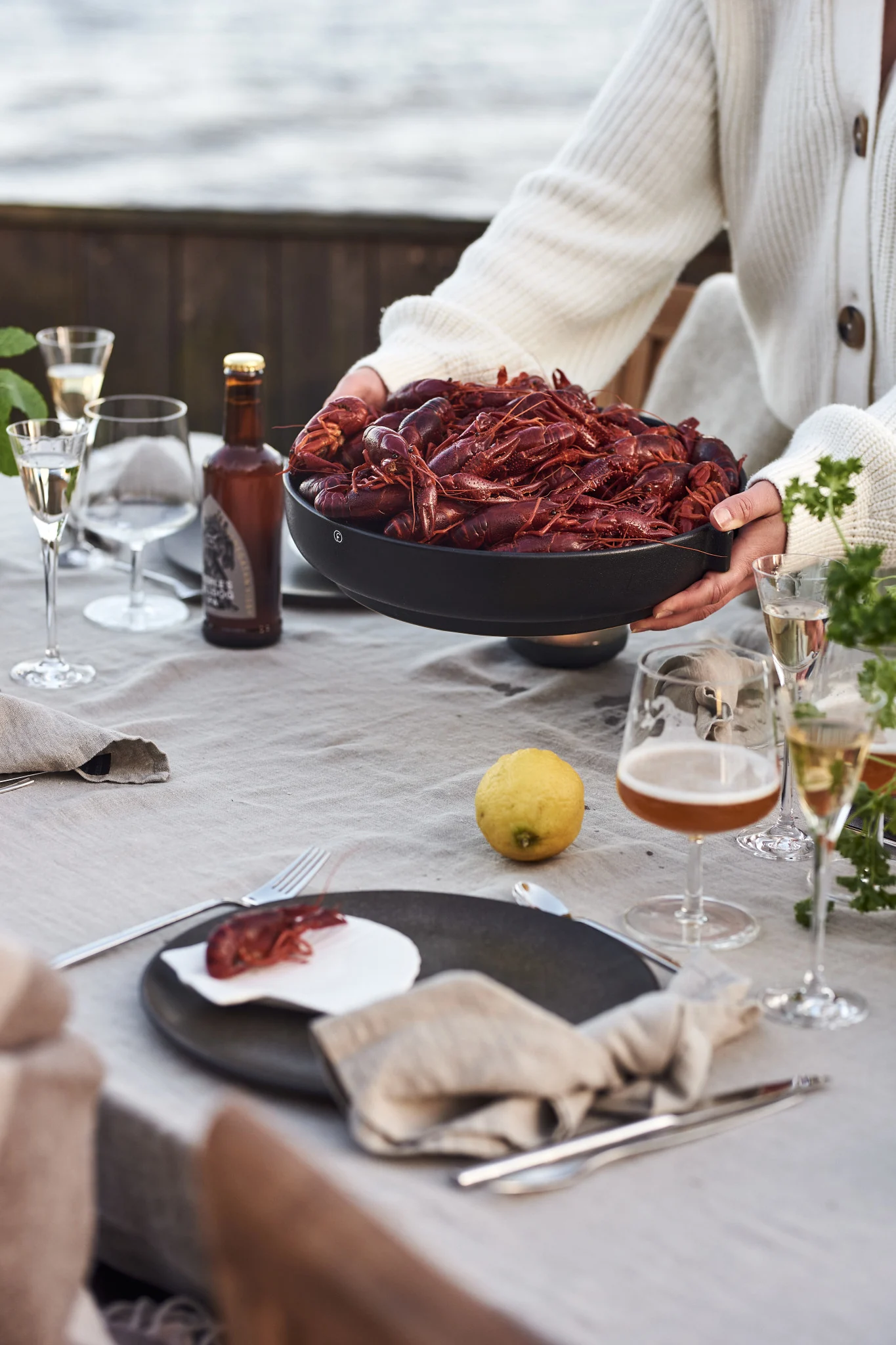 If you have never experienced a Swedish crayfish party you should add it to your summer bucket list. Here you see a pair of hands placing a bowl filled with crayfish on the table. 