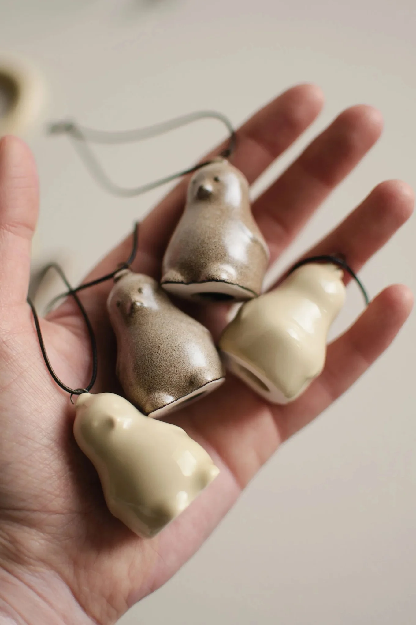 Hand holding four small ceramic bird ornaments, two speckled brown, two creamy white, with strings.