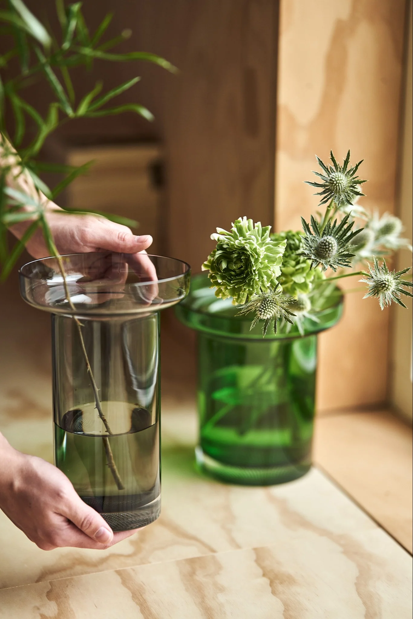 Hands place the grey rose vase from the Limelight collection for Kosta Boda on a plywood bench. 