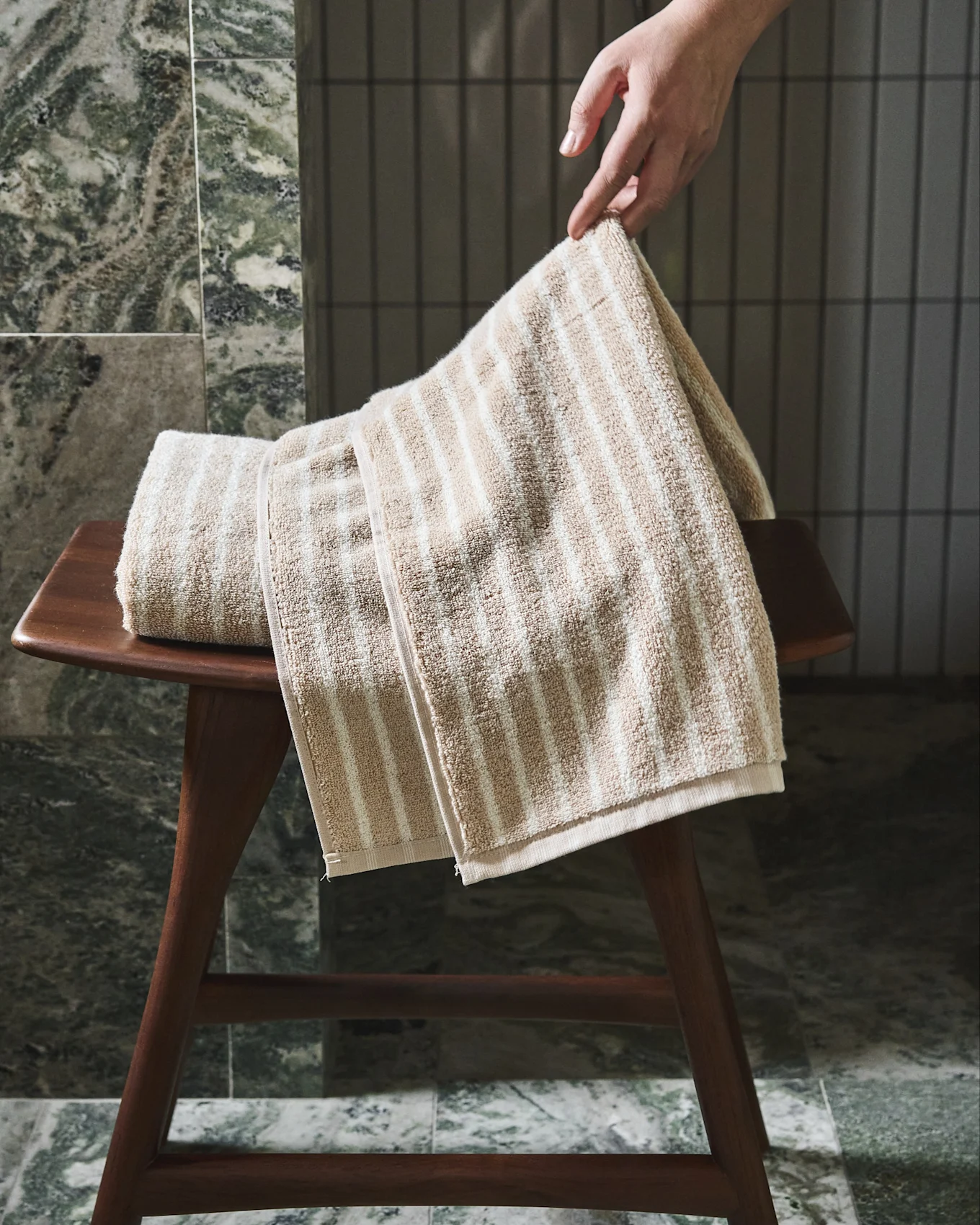 Hand adjusting a beige and white striped towel on a wooden stool.