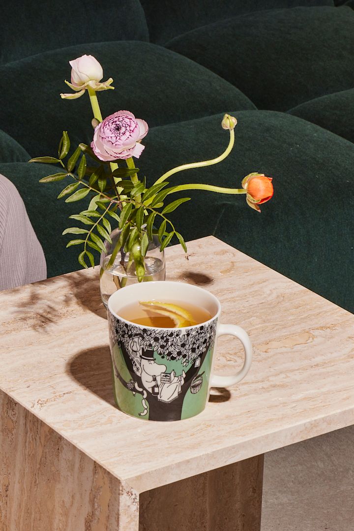 The green Moomin cup stands on a coffee table with coffee.