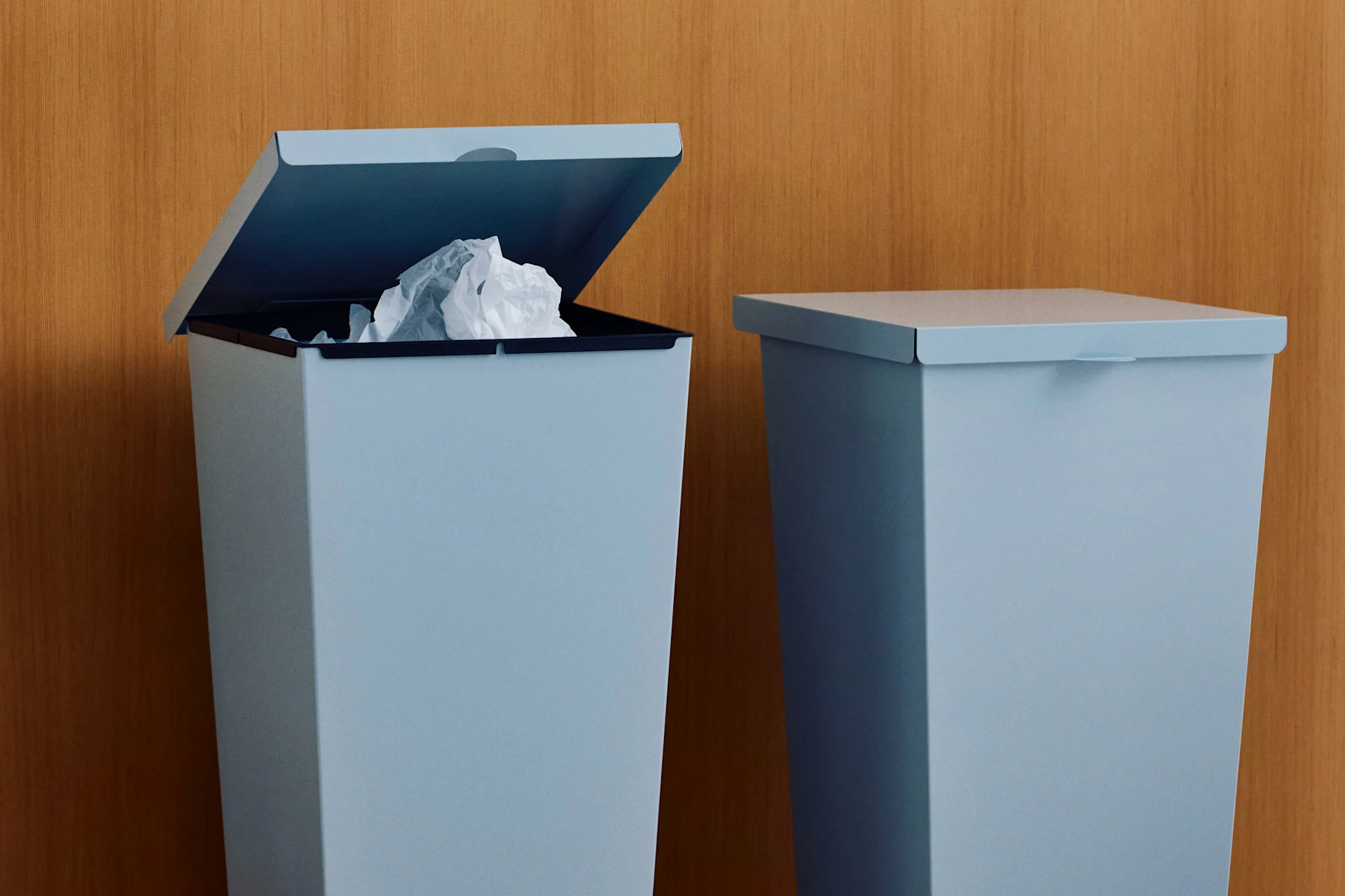 Two light blue trash cans against a wooden wall, one open with crumpled paper.