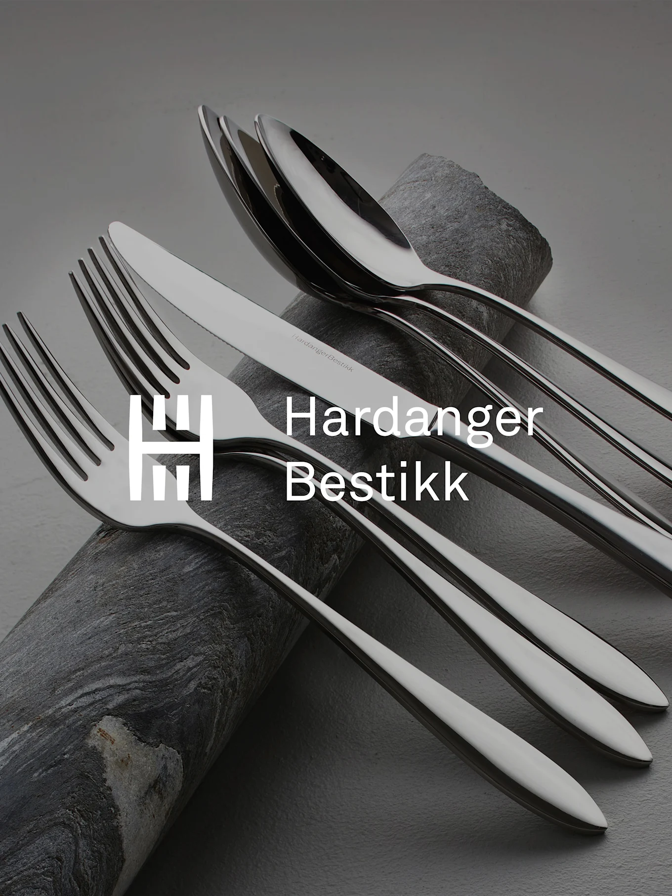 Shiny stainless steel cutlery set, including forks, knives, and spoons, artfully arranged on dark, textured stone.