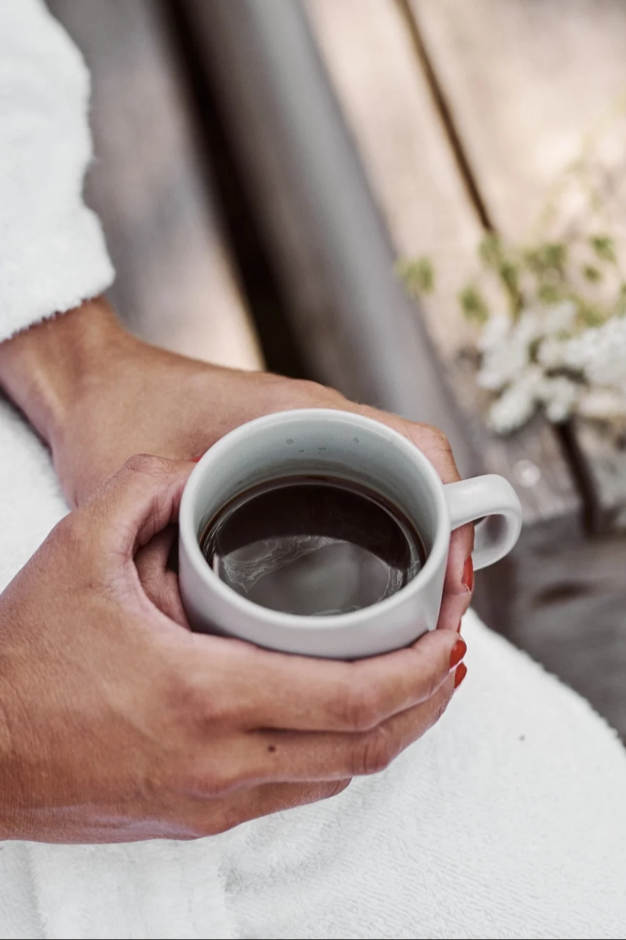 Be sure to put a Swedish fika in the sun on your summer bucket list. Here you see hands hold a warm mug of coffee. 