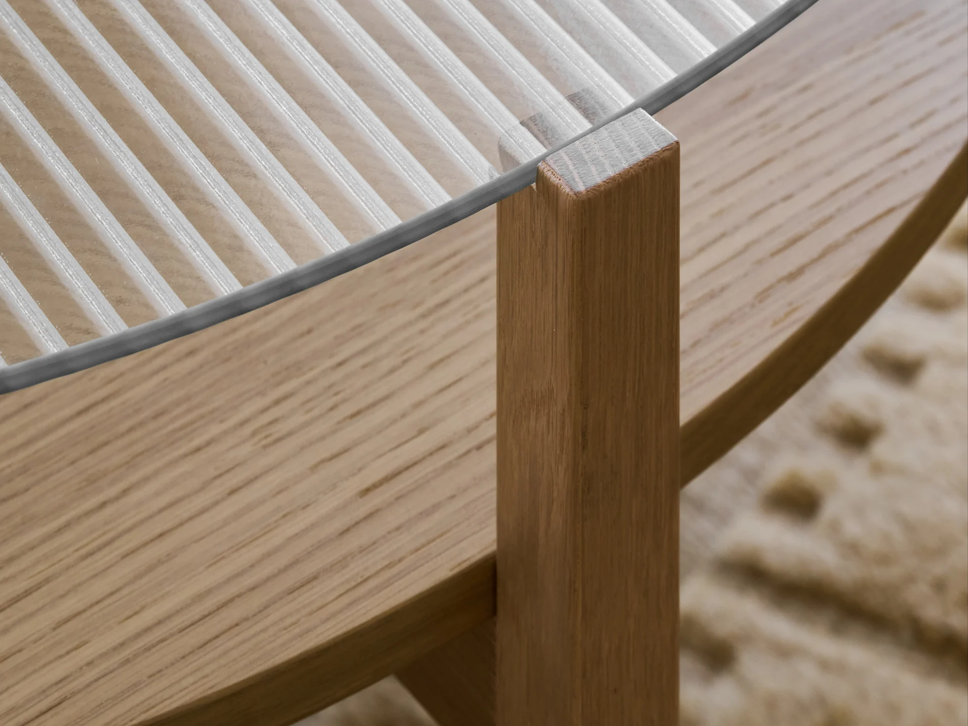 Close-up of a table with a ribbed glass top and a light brown wooden leg.