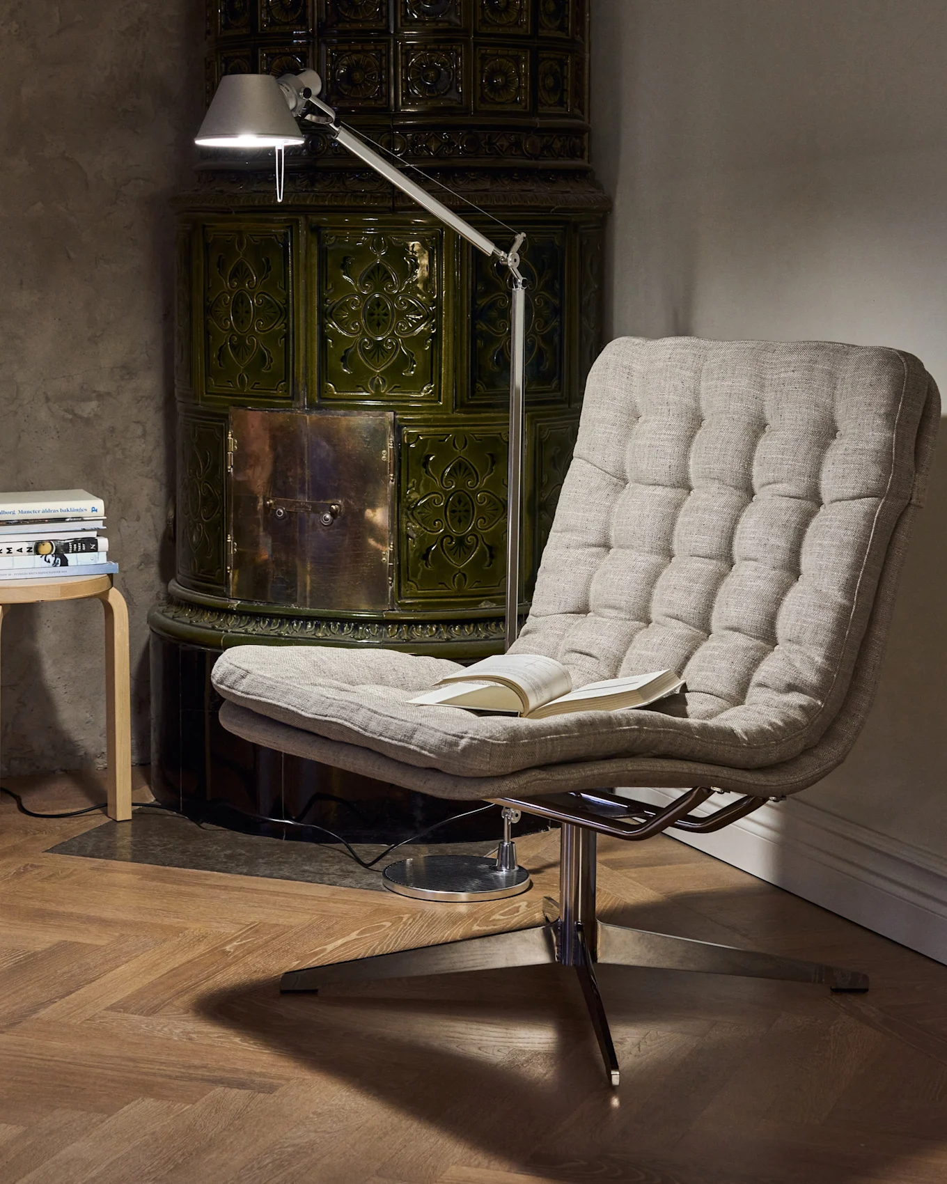 Cozy reading nook featuring a tufted armchair, an adjustable floor lamp, and a dark green tiled stove.