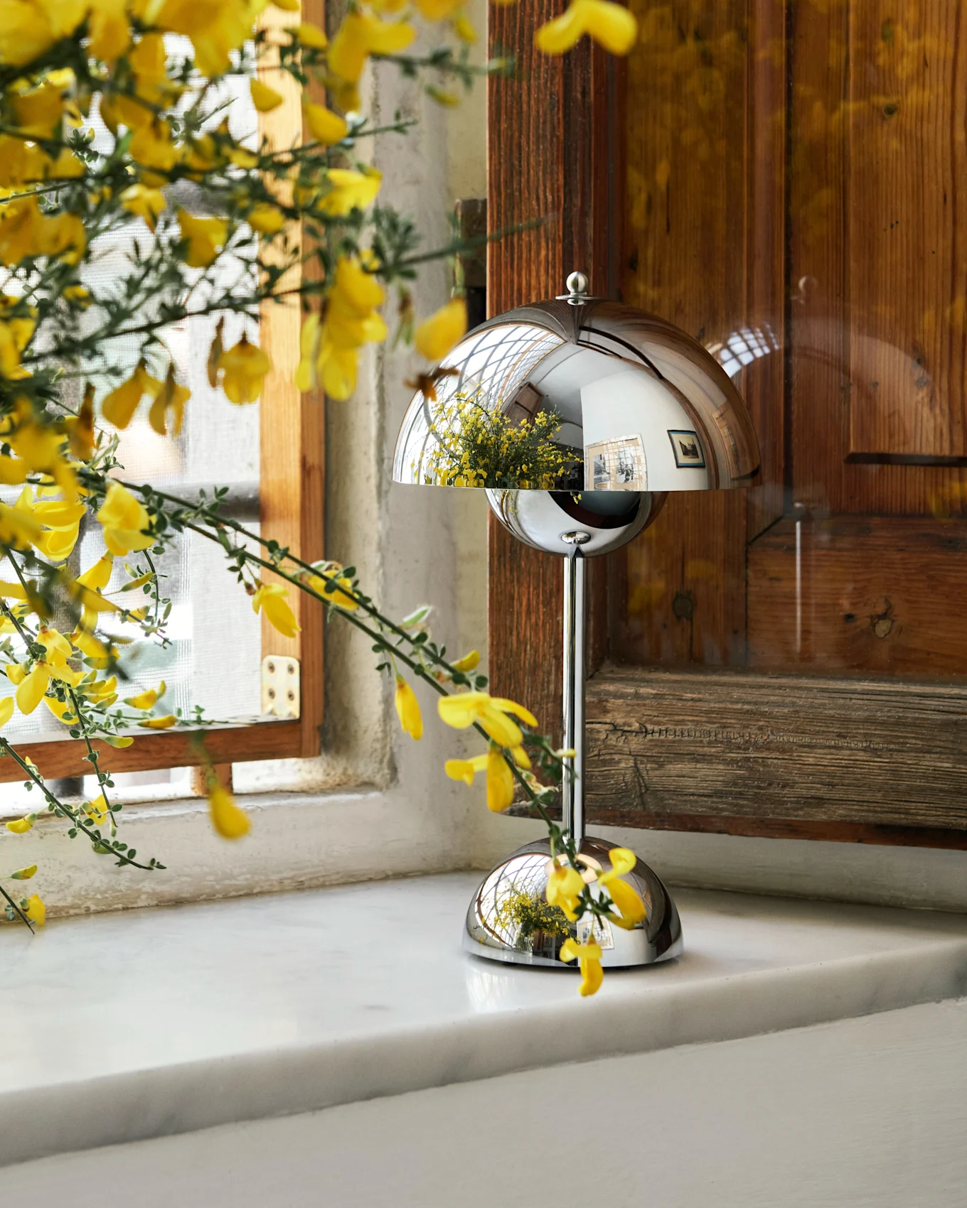 Yellow flowers in a vase next to a reflective dome-shaped lamp on a white windowsill.