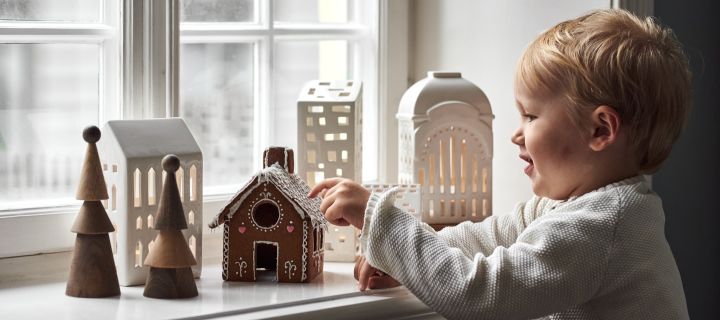 How to decorate with traditional Scandinavian Christmas decorations - here you see a young boy eating a gingerbread house on the windowsill surrounded by other Gingerbread house style candle holders.