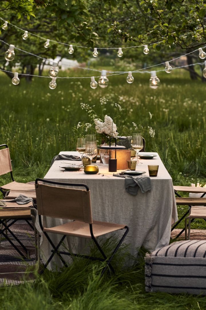 A summer table setting in long grass with cordless table lamps lighting up the table. 