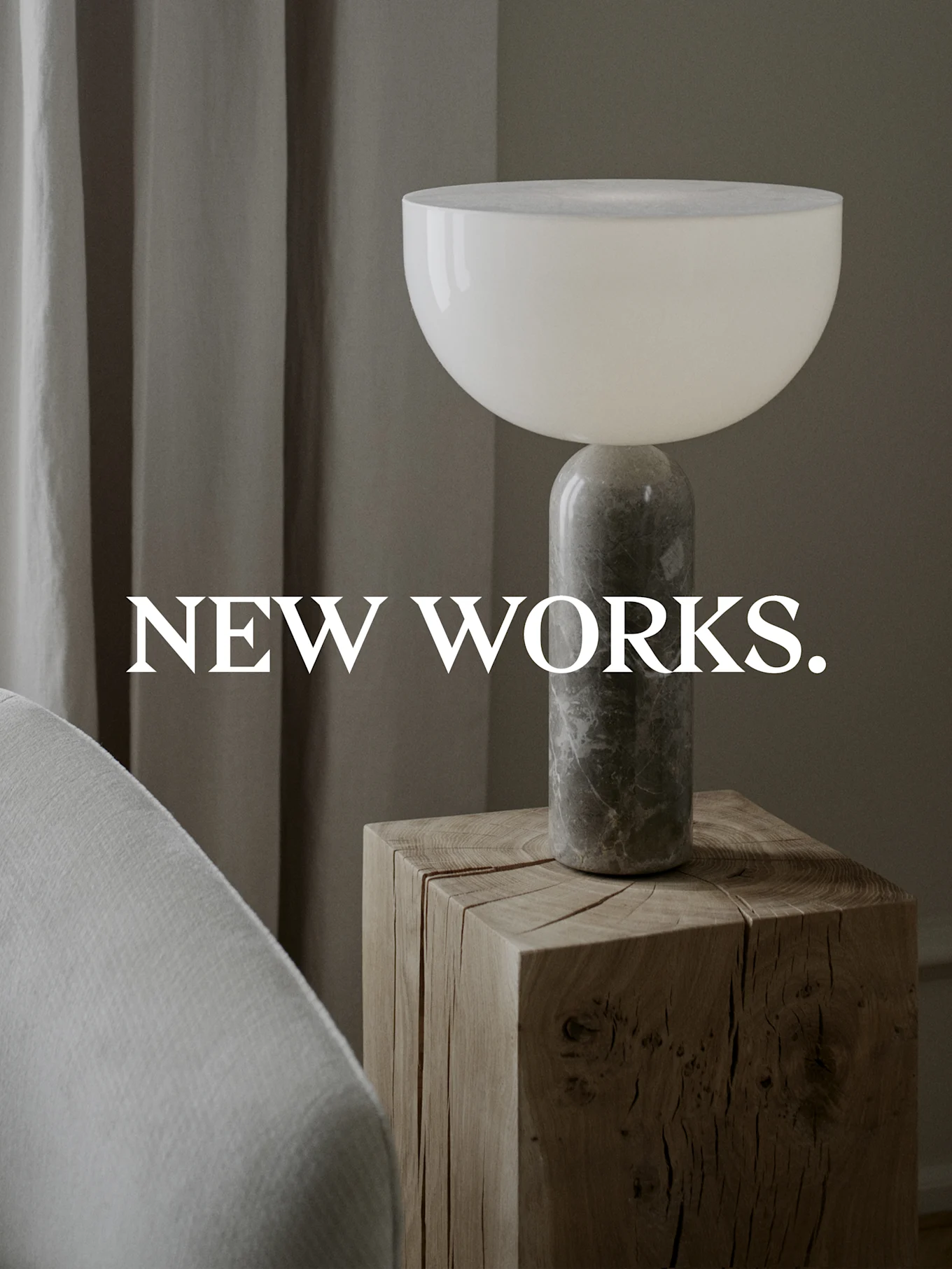 Modern table lamp with a white bowl shade and a marbled grey cylindrical base, on a rustic wooden block table. Text: NEW WORKS.