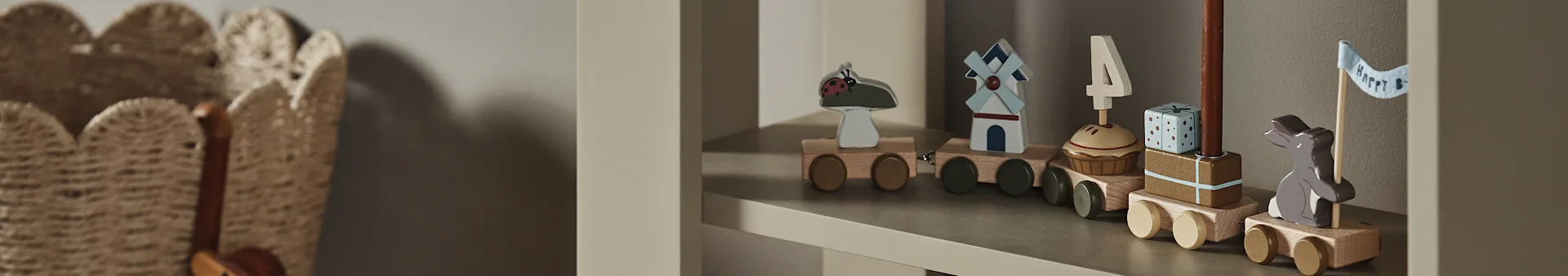 A wooden toy train on a shelf, with cars featuring a ladybug, windmill, cupcake with '4' candle, gift, and a bunny holding a "Happy B" flag.