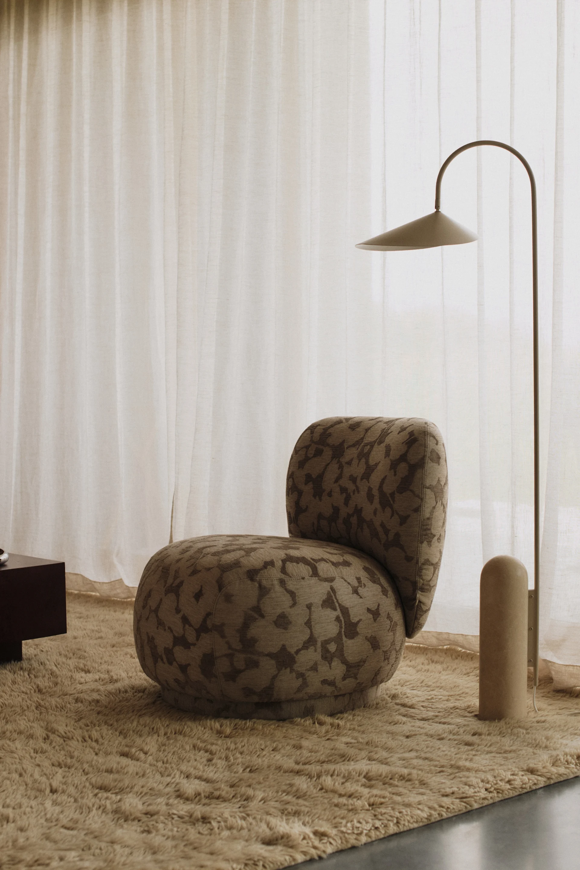 An armchair upholstered in floral fabric stands in a pared-back room together with a floor lamp that reflects the interior design trends of 2026.