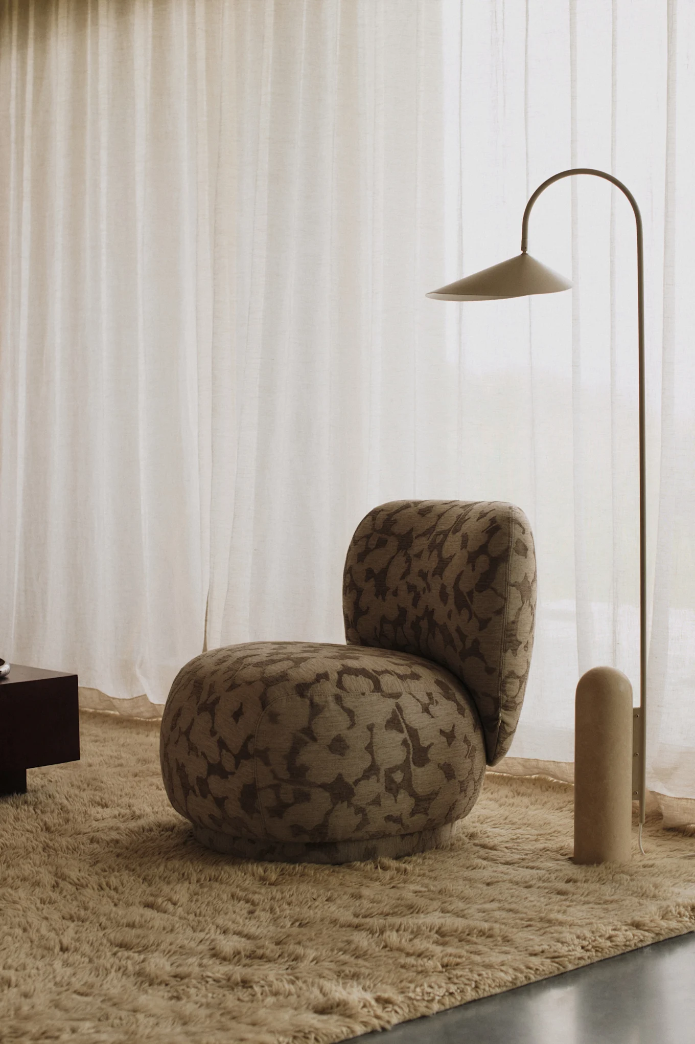 An armchair upholstered in floral fabric stands in a pared-back room together with a floor lamp that reflects the interior design trends of 2026.