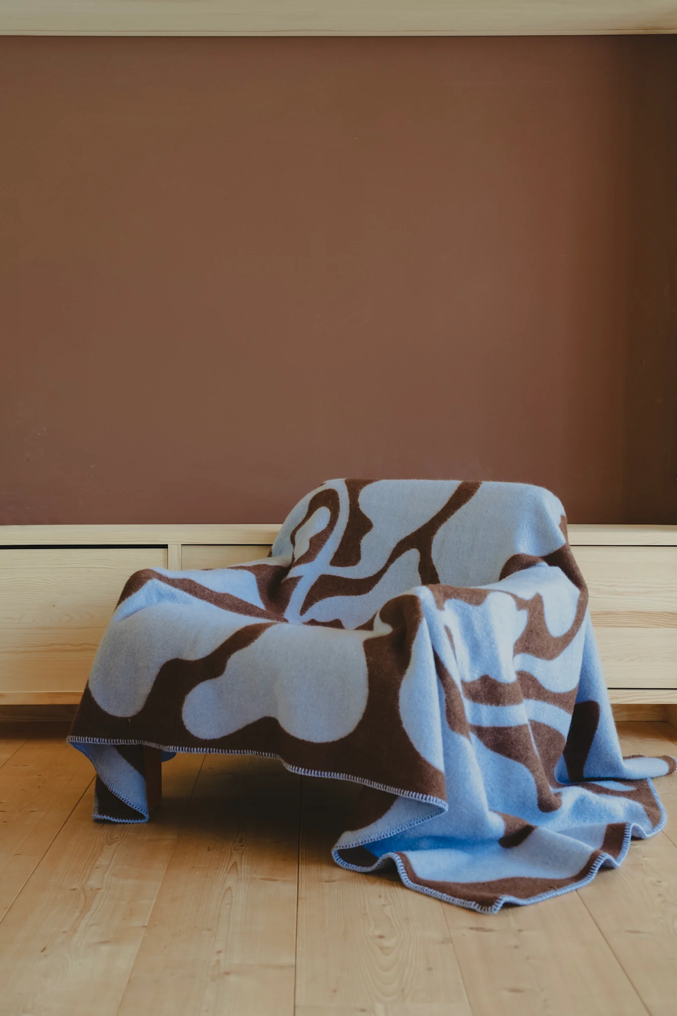The brown blue patterned Leaves blanket from Fine little day lies over an armchair and is one of the 2025 interior design trends thanks to its colour scheme.