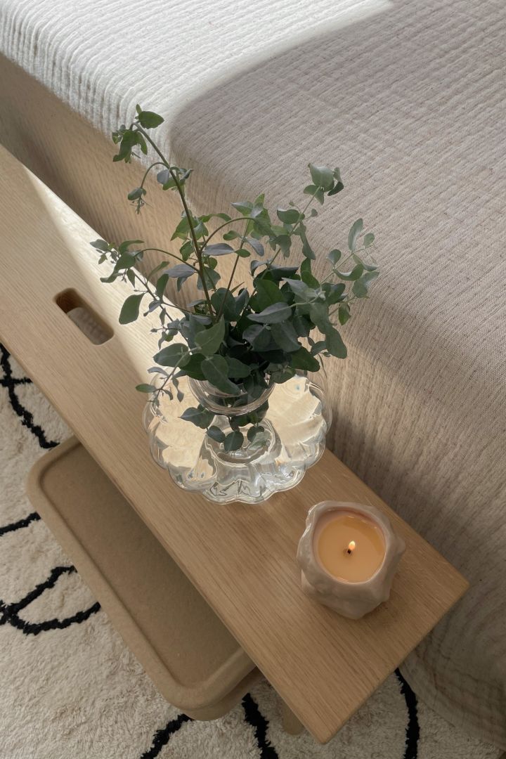 Fresh flowers in the Balloon vase from Louise Roe Copenhagen and a scented candle from Ferm Living seen from above in a Scandinavian bedroom.