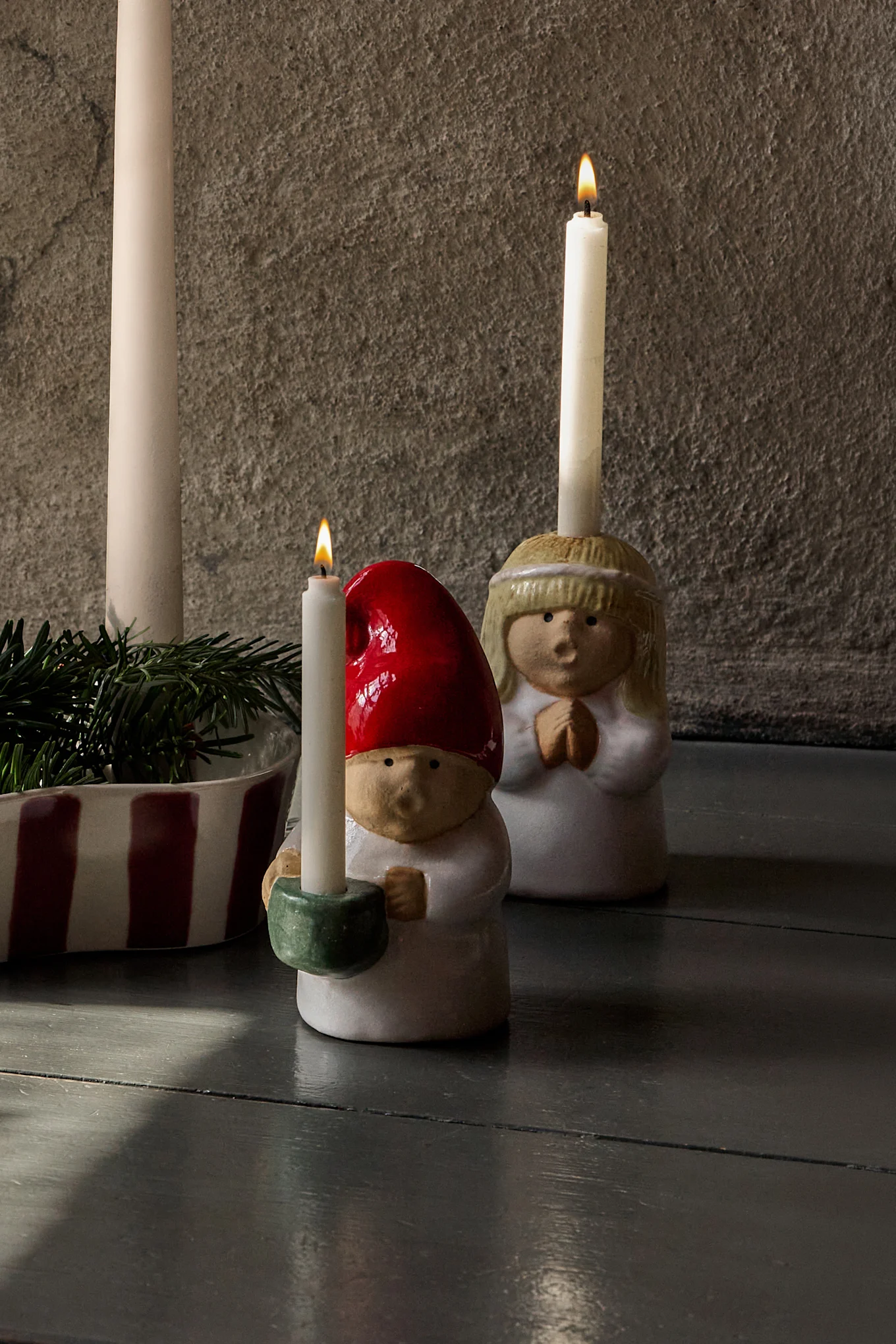 Advent display: four unlit candles in a striped holder with pine, flanked by ceramic angel and gnome figures with lit candles.