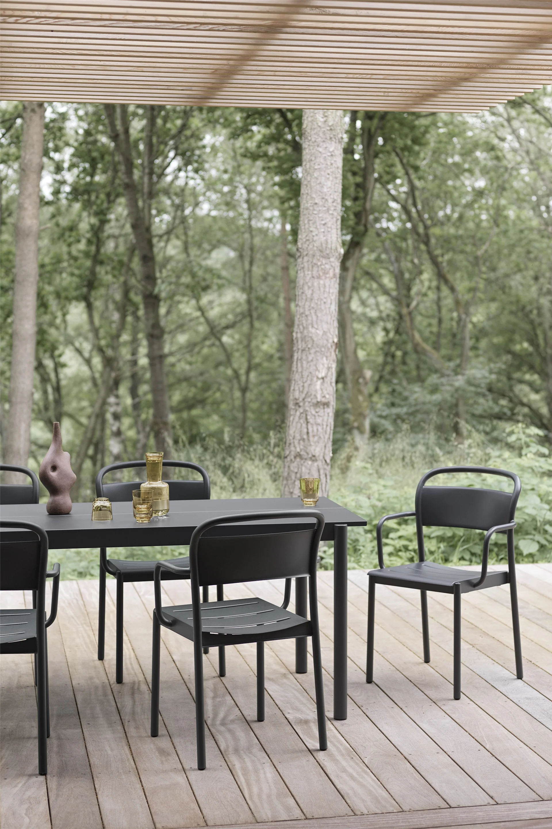 A covered wooden terrace with a table and chairs in black from the Linear collection by Muuto.